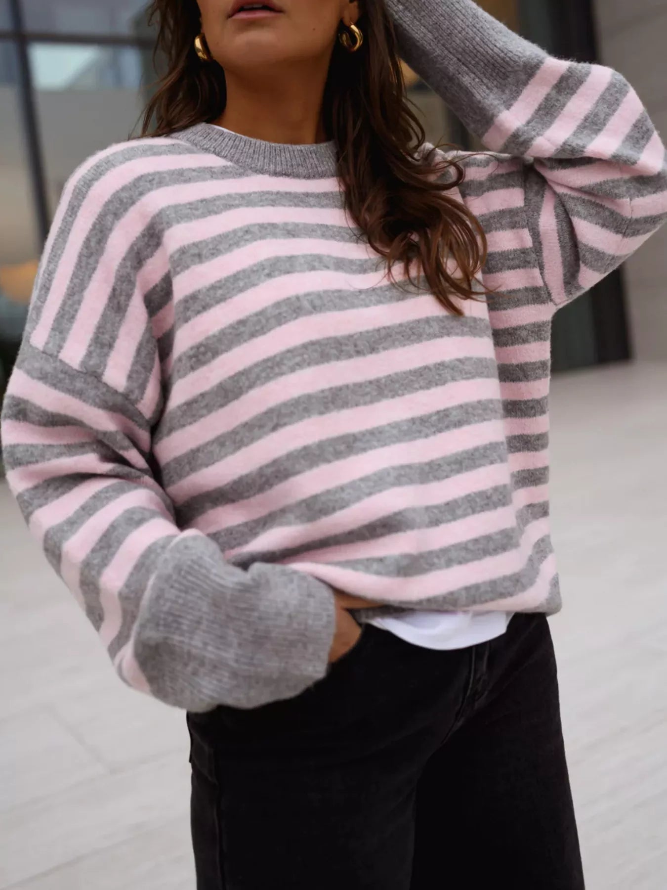 On-model front view of a gray and pink striped crew neck sweater, arm raised