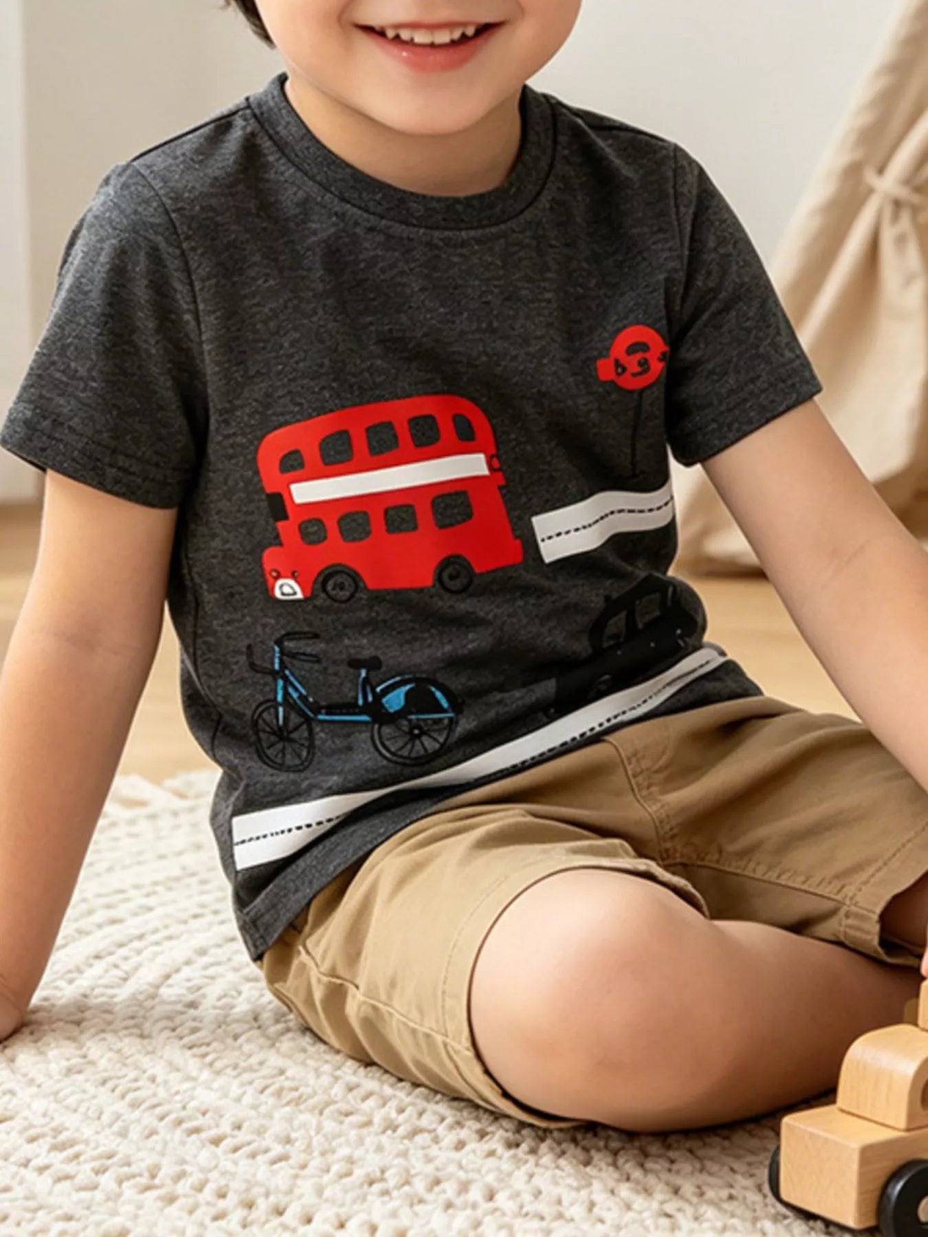 Dark gray children's short sleeve t-shirt with red double decker bus graphic worn indoors