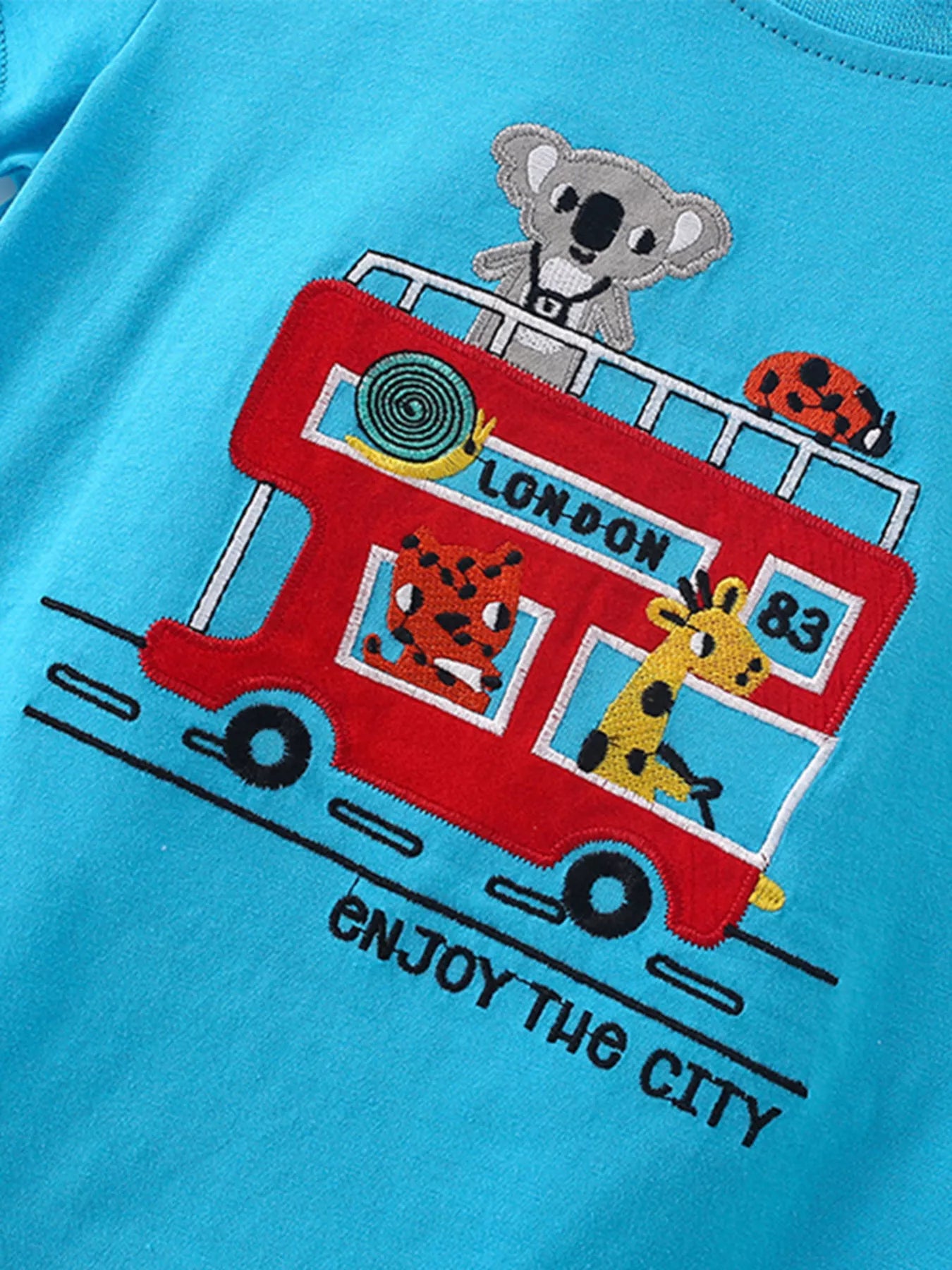Angled close-up of red bus embroidery with cartoon animals on sky blue children's tee