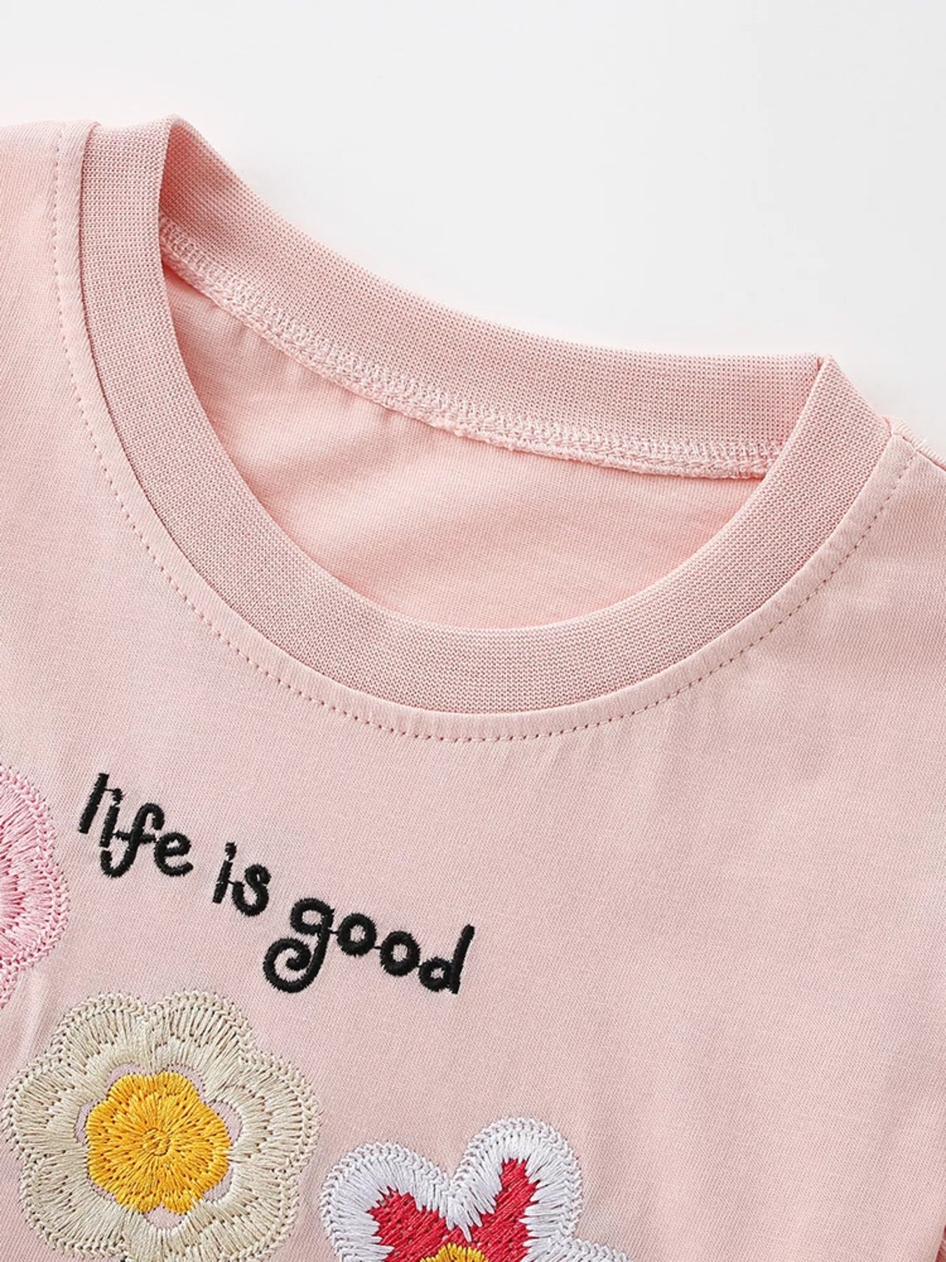 Close up of blush pink children's t-shirt round neckline with embroidered flower and lettering detail