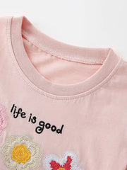 Close up of blush pink children's t-shirt round neckline with embroidered flower and lettering detail