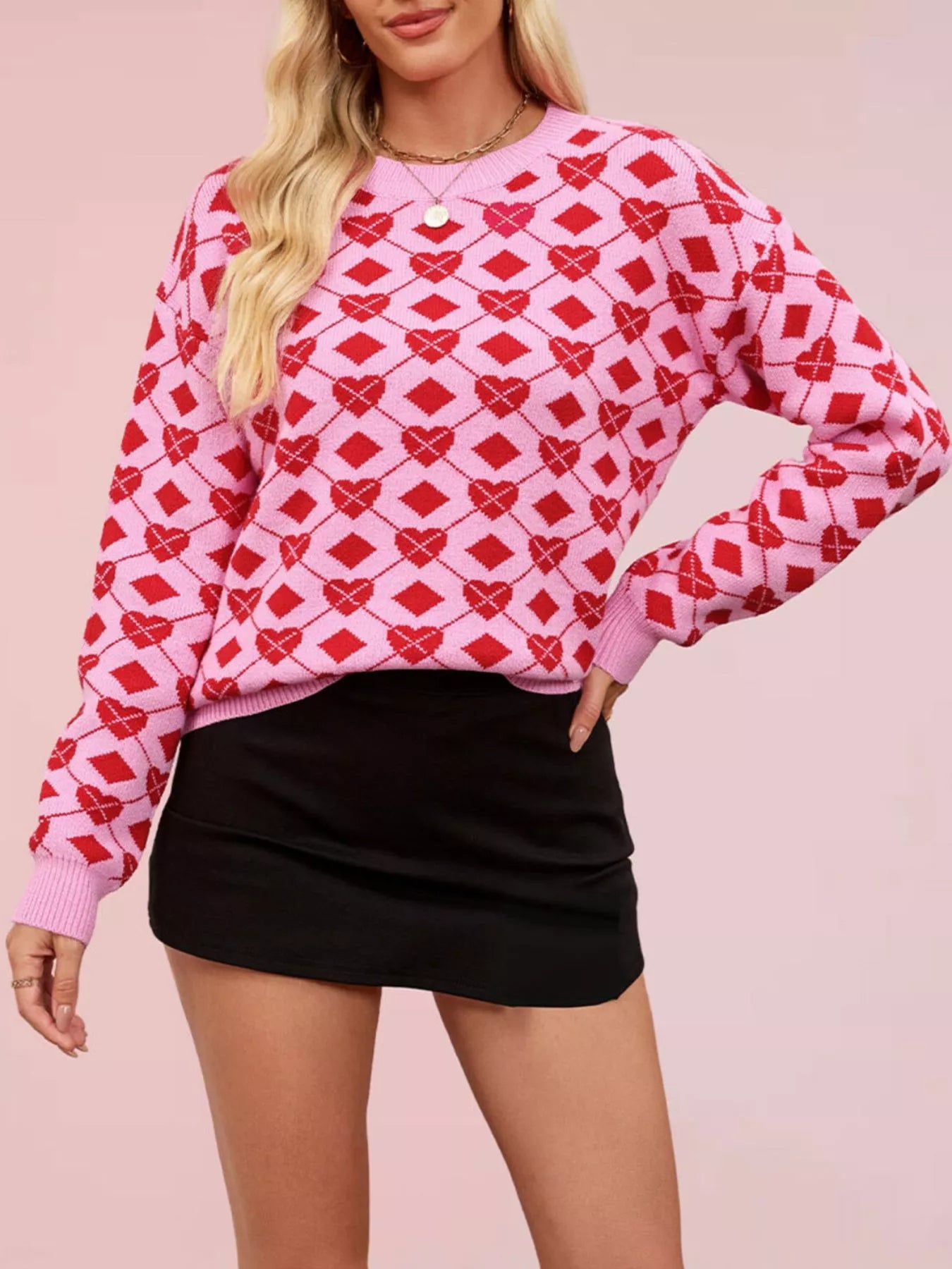 Front view of a pink knit sweater with red heart argyle pattern, hand on hip