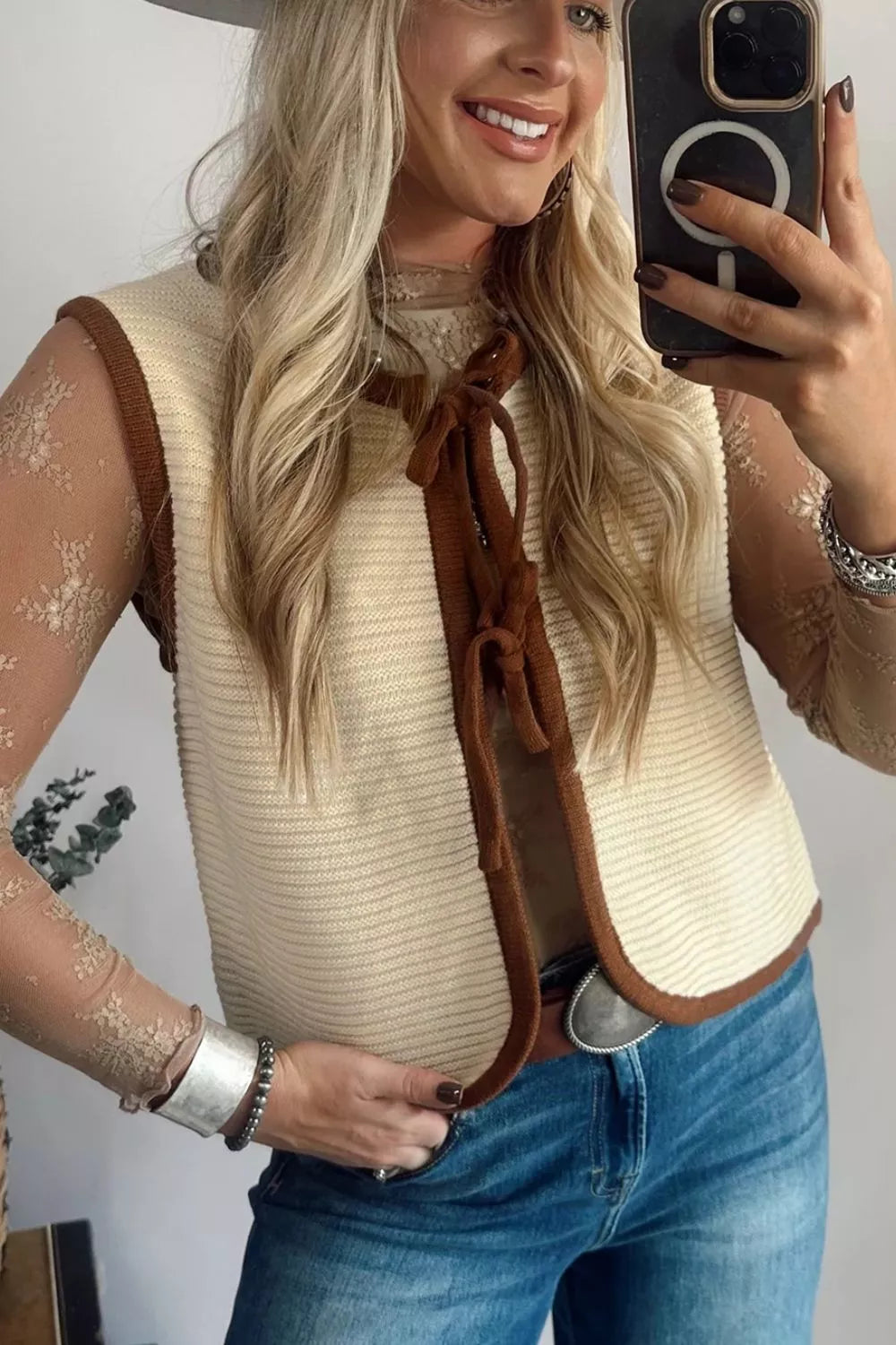On-model mirror selfie of a beige tie front sweater vest with brown contrast trim