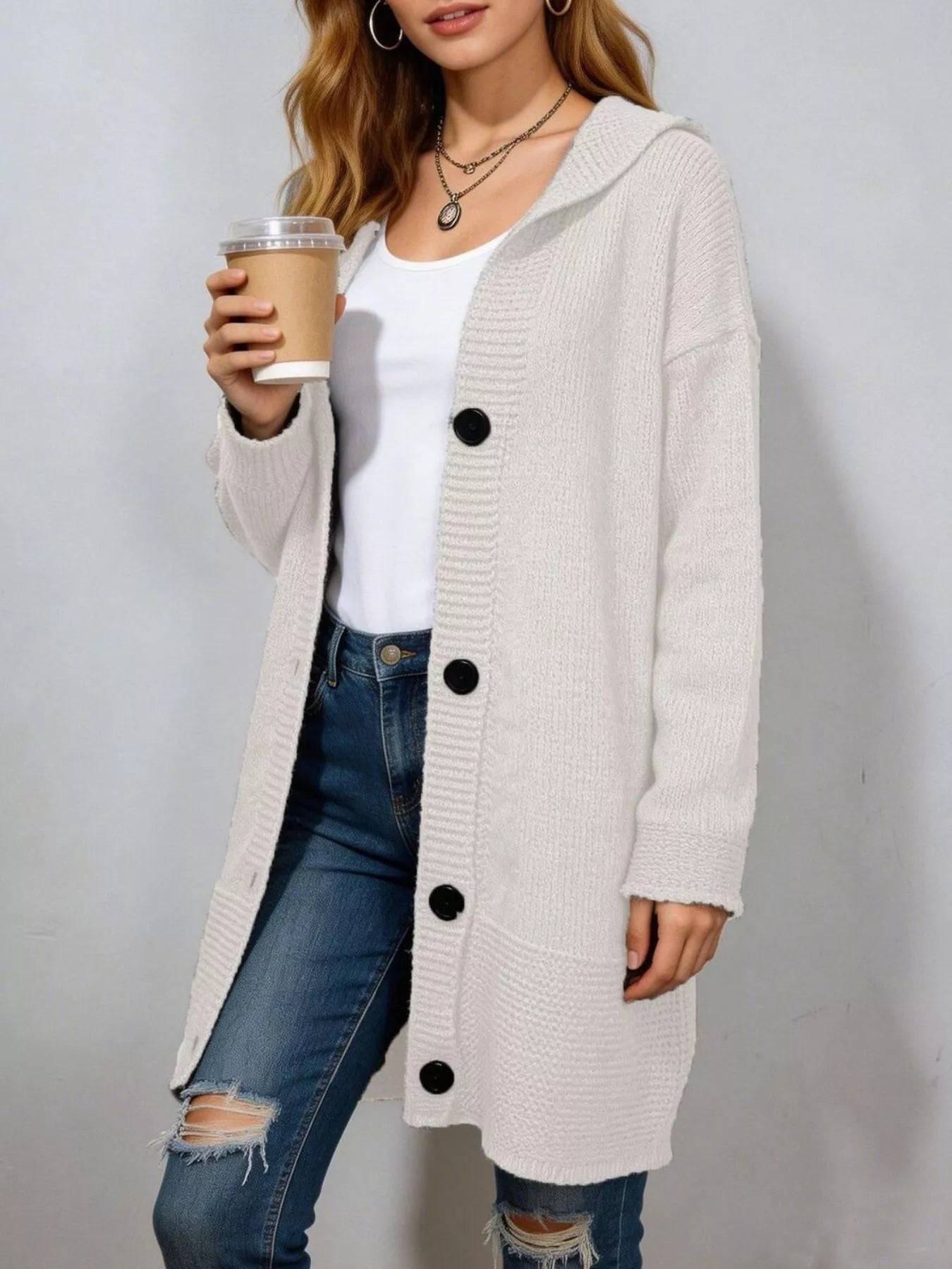 Long cream hooded knit cardigan with black buttons worn open indoors