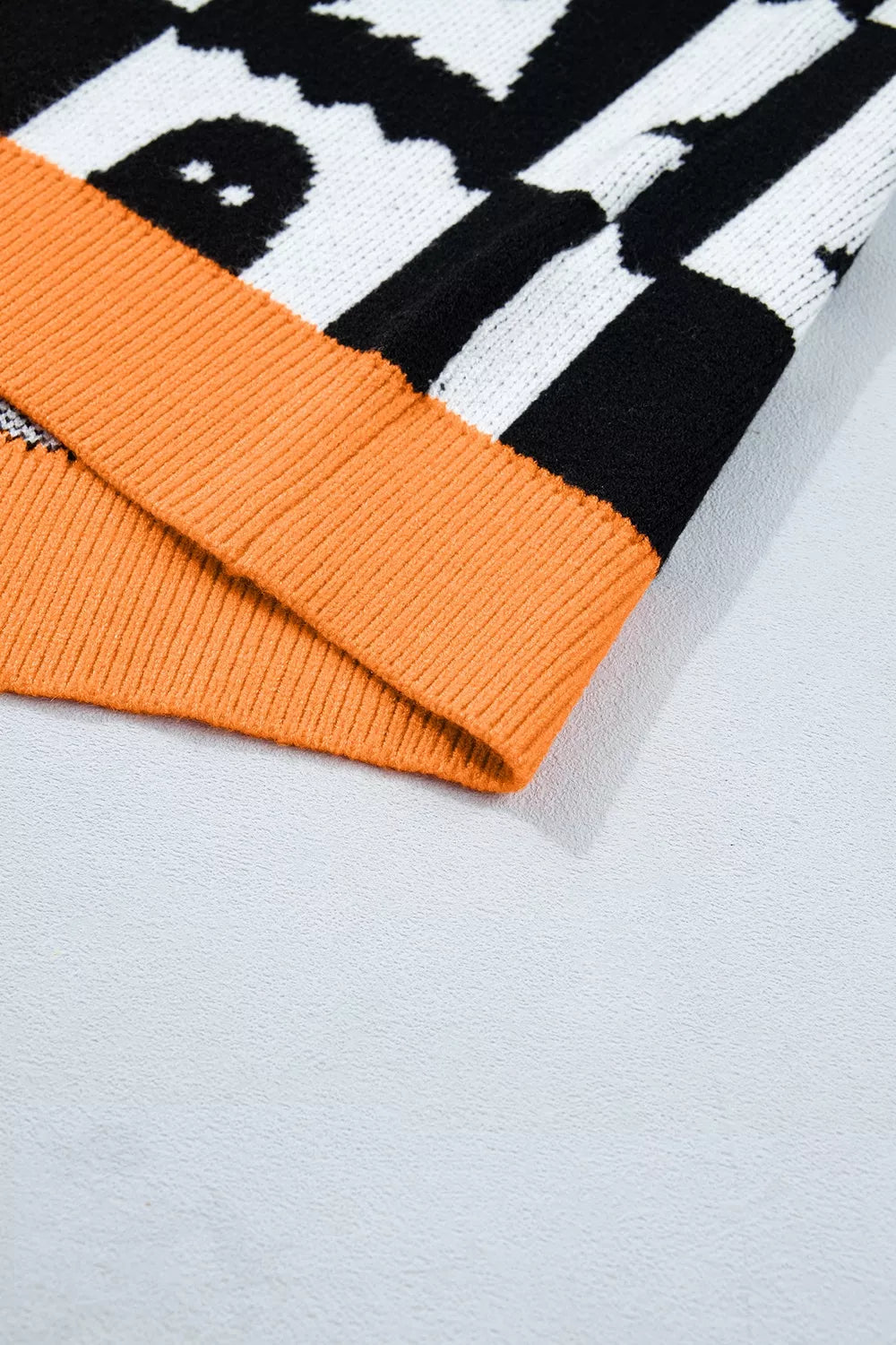 Close up of an orange ribbed hem on a black and white ghost checkerboard sweater