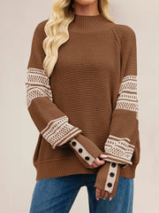 Front view of a brown waffle knit sweater with cream patterned sleeves and button cuffs, hands crossed.
