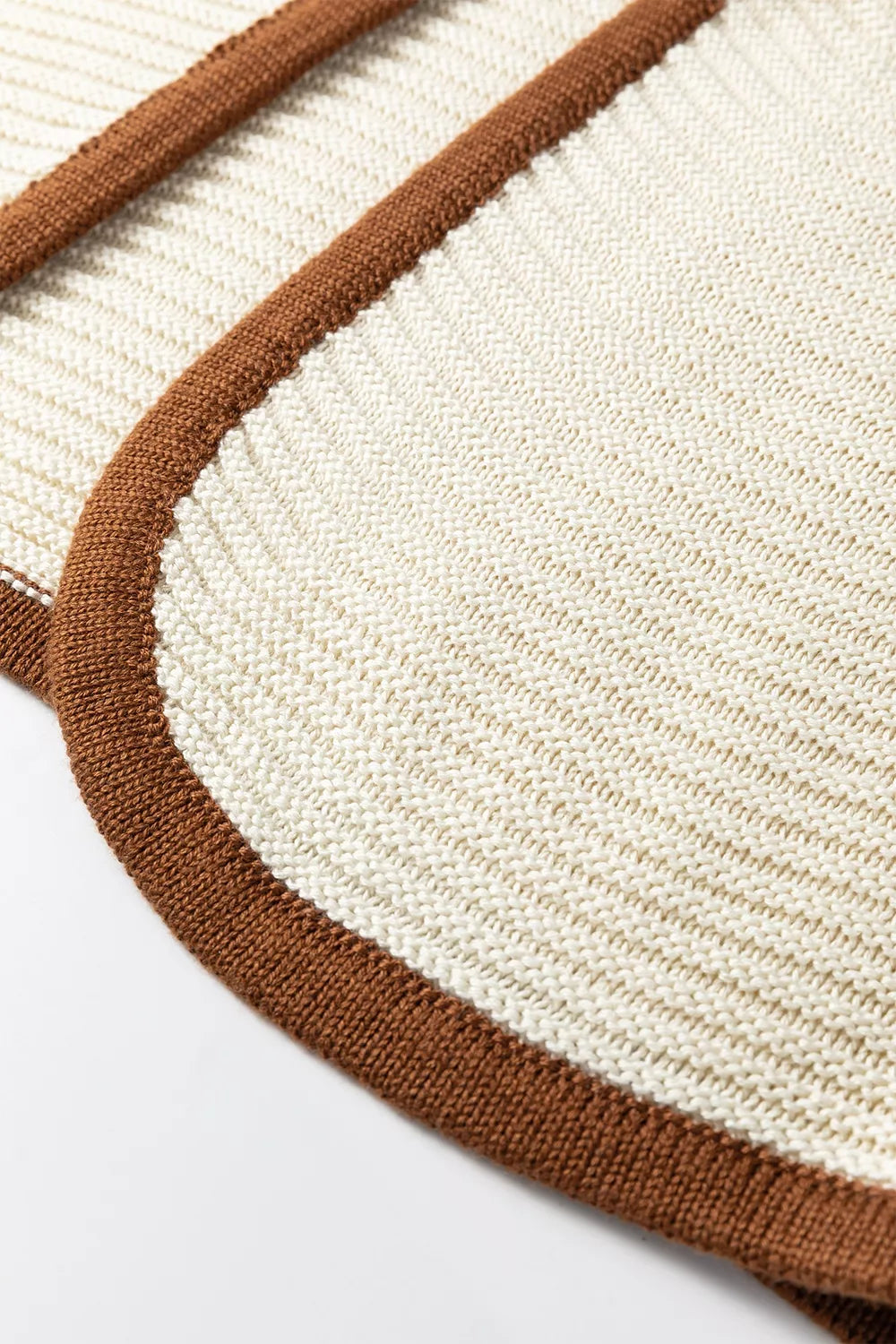 Close up detail of a beige sweater vest curved hem with brown contrast trim