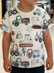White children's short sleeve t-shirt with all over cartoon trucks excavators trees and stars worn indoors