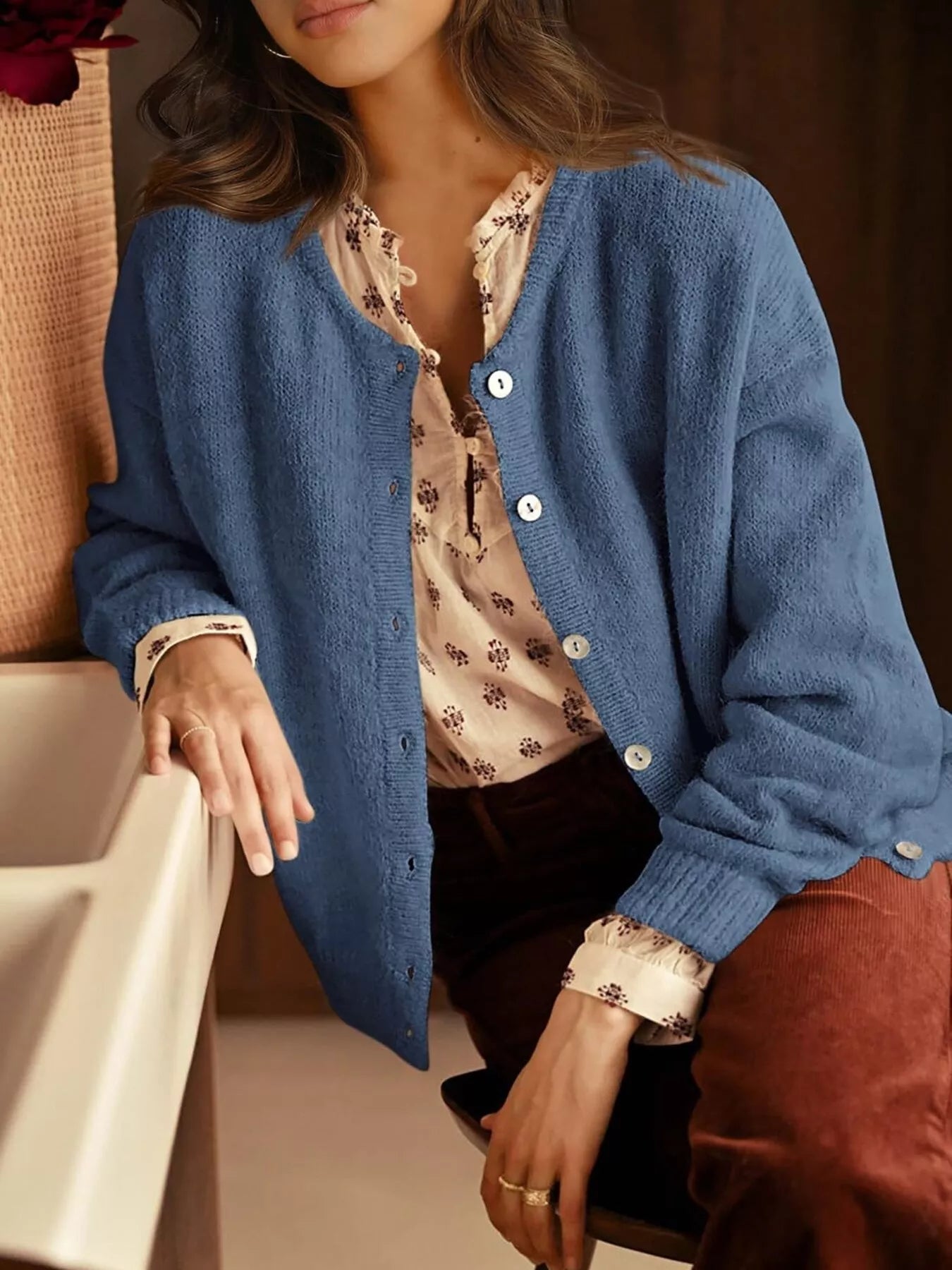 Open haze blue button down cardigan worn over a floral blouse while seated indoors