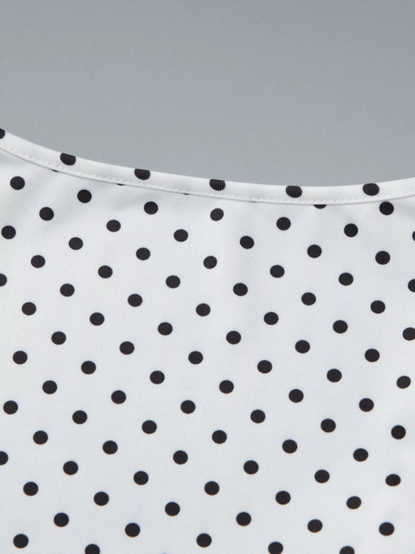 Close-up detail of a white polka dot top showing the ruched V-neckline and upper front.
