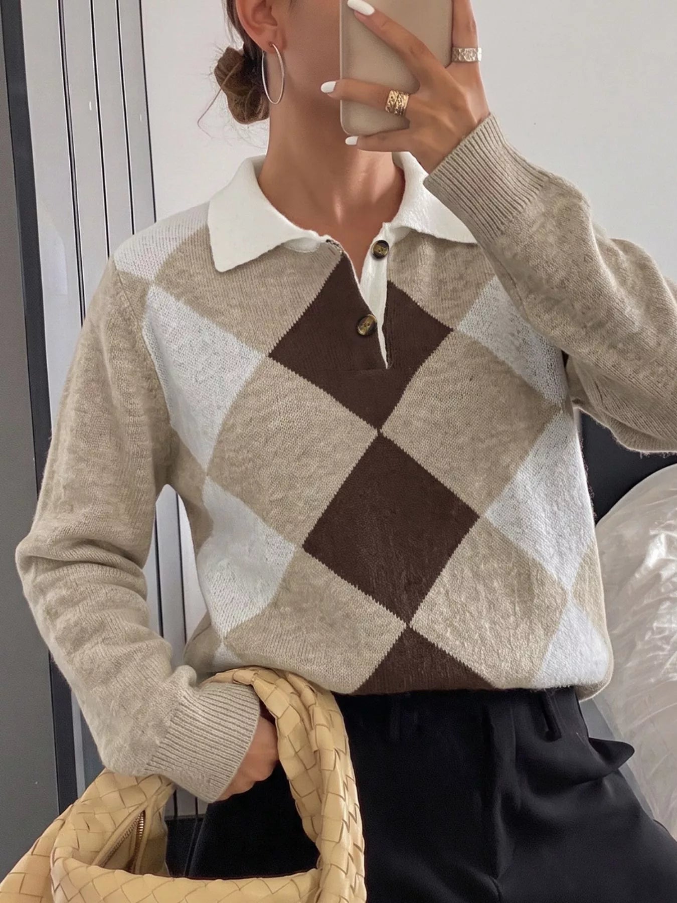Mirror selfie front view of the argyle polo sweater with a hand holding a woven bag