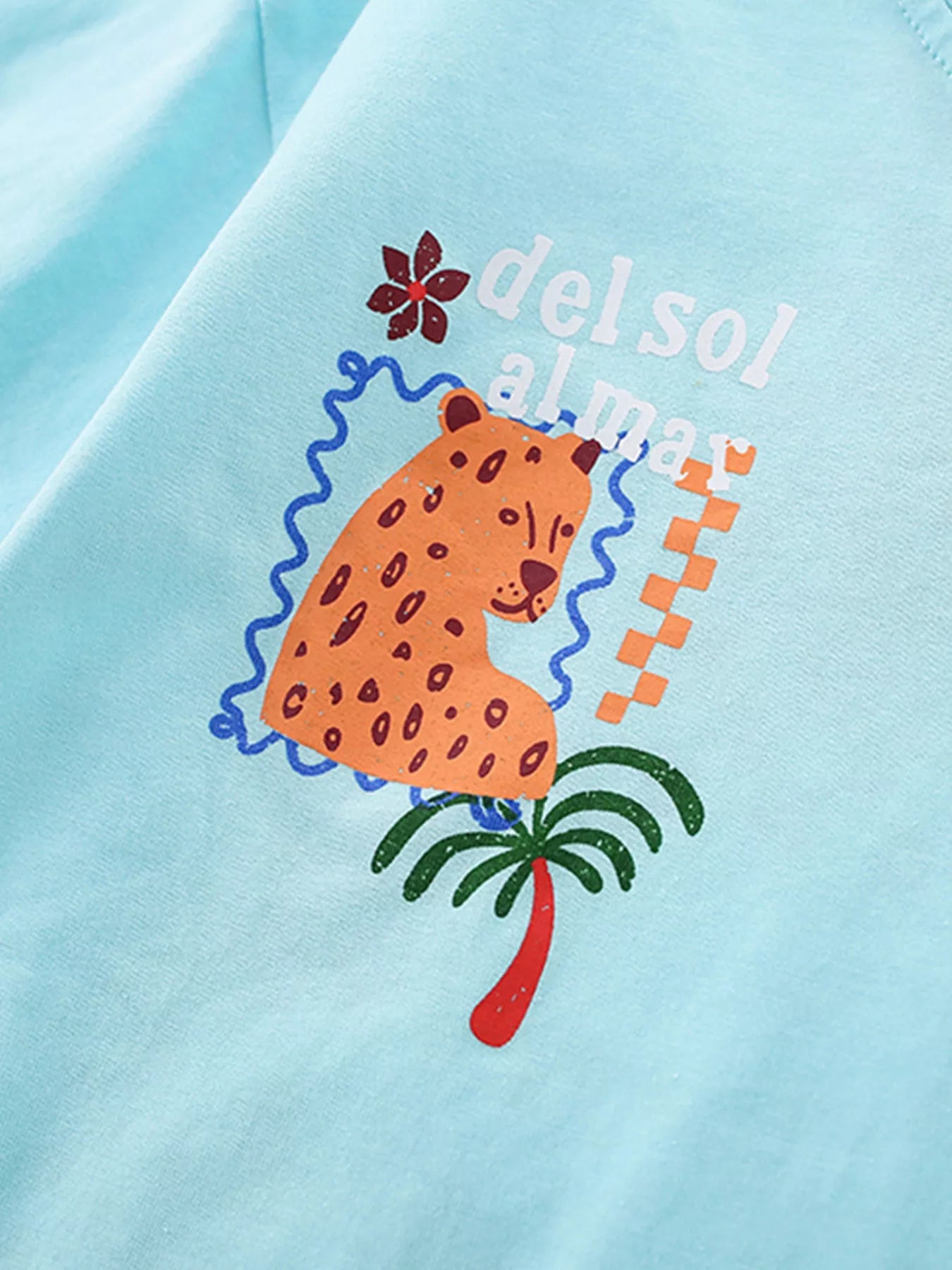 Close-up of the cartoon leopard and palm tree chest graphic on a mint blue T-shirt
