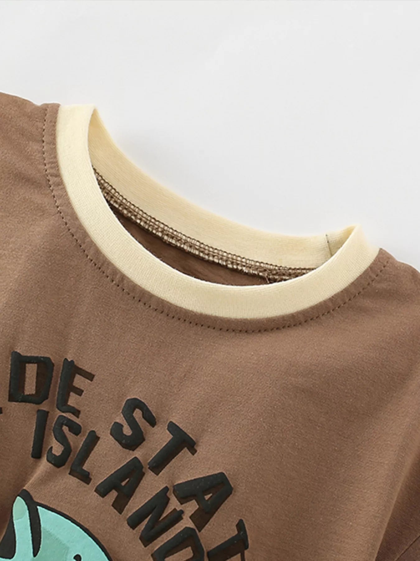 Close-up of cream contrast crew neckline and stitching on caramel children's fishing graphic t-shirt