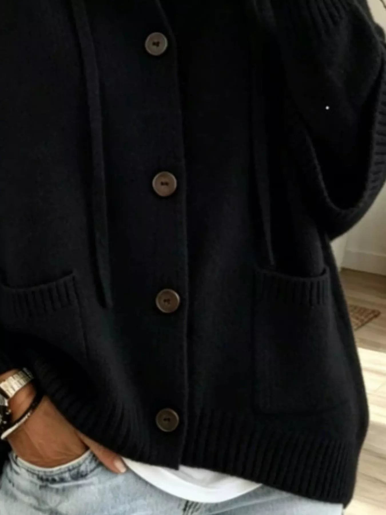 Detail view of the black cardigan showing brown buttons, patch pockets and ribbed hem