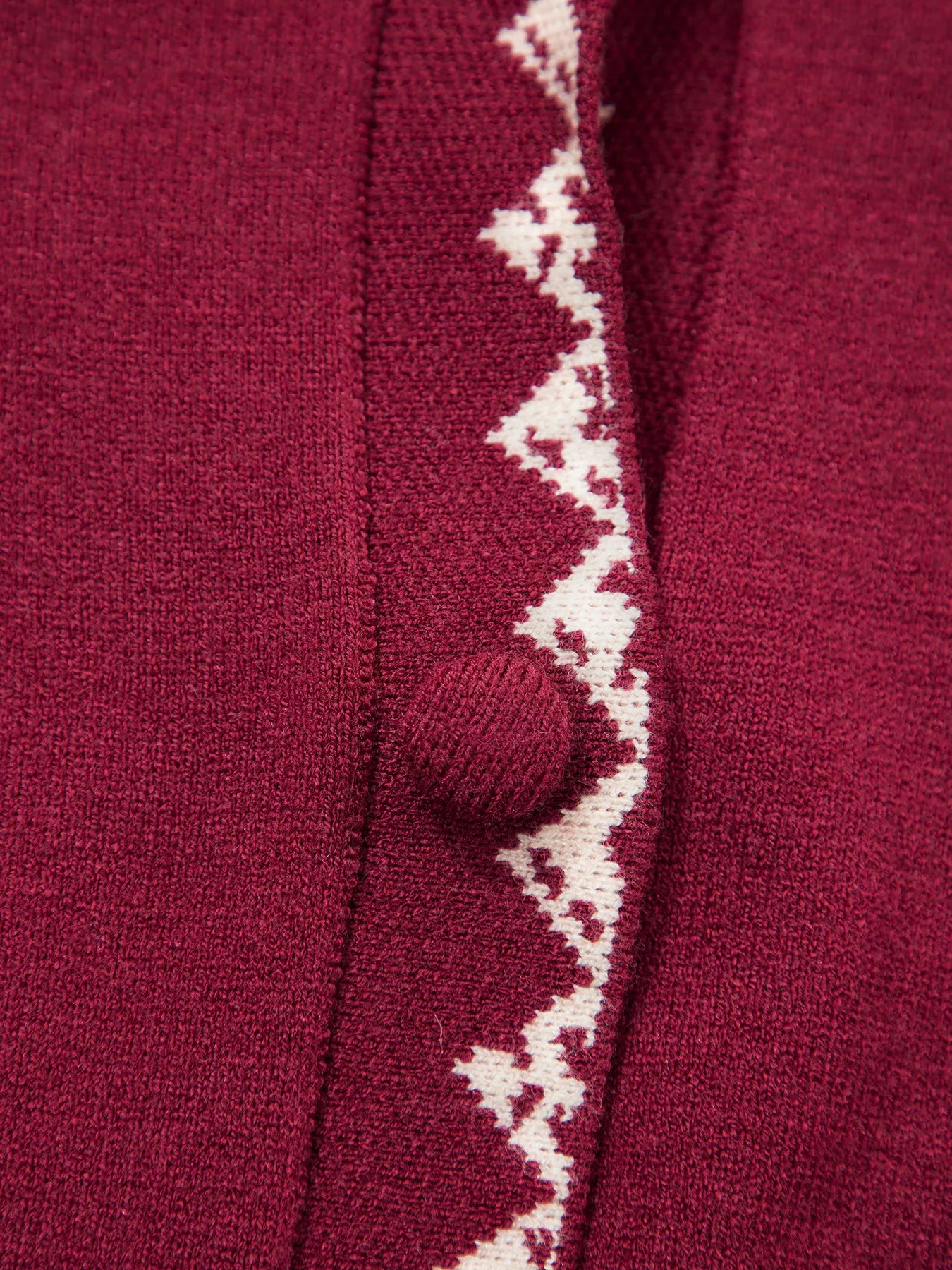 Extreme close view of the burgundy cardigan button and cream zigzag trim