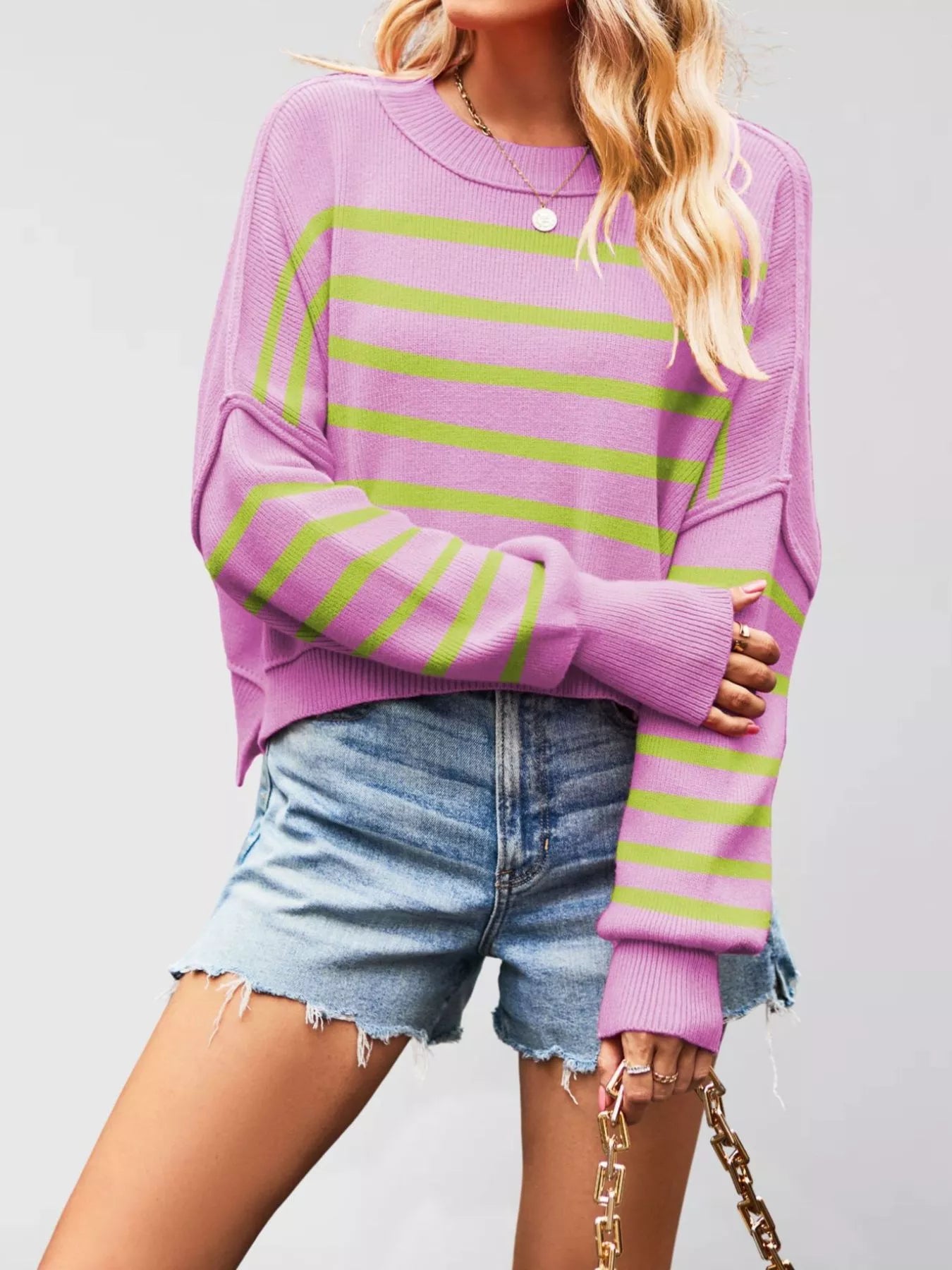 Front view of a purple sweater with green stripes, crew neck, and dropped shoulders worn with denim shorts.