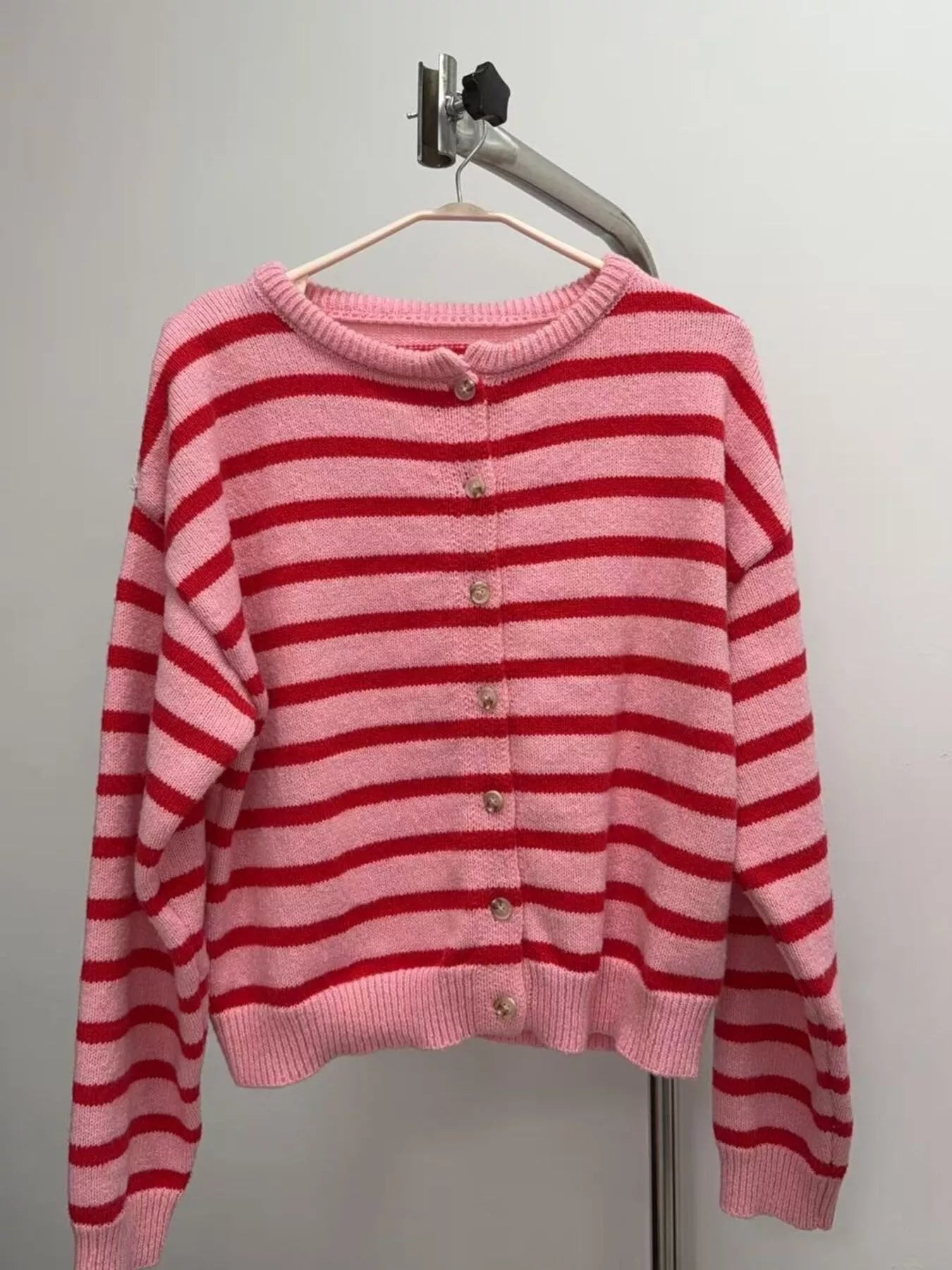 Pink and red striped button down cardigan hanging on a hanger against a plain wall