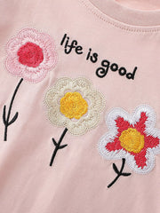 Close up of three embroidered flowers in pink cream and red on blush pink children's t-shirt