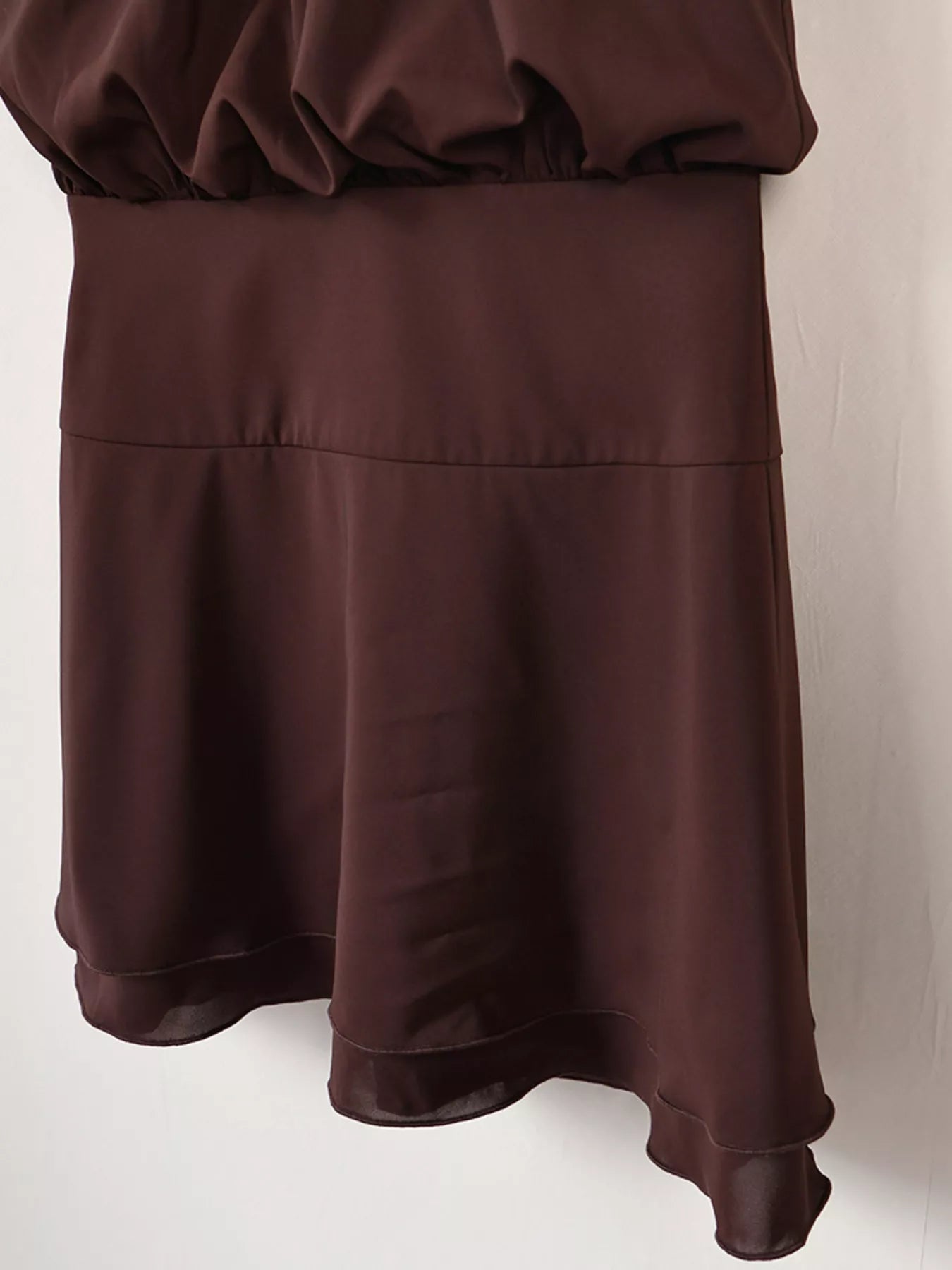 Brown mini dress detail showing waistband and tiered flared skirt on hanger