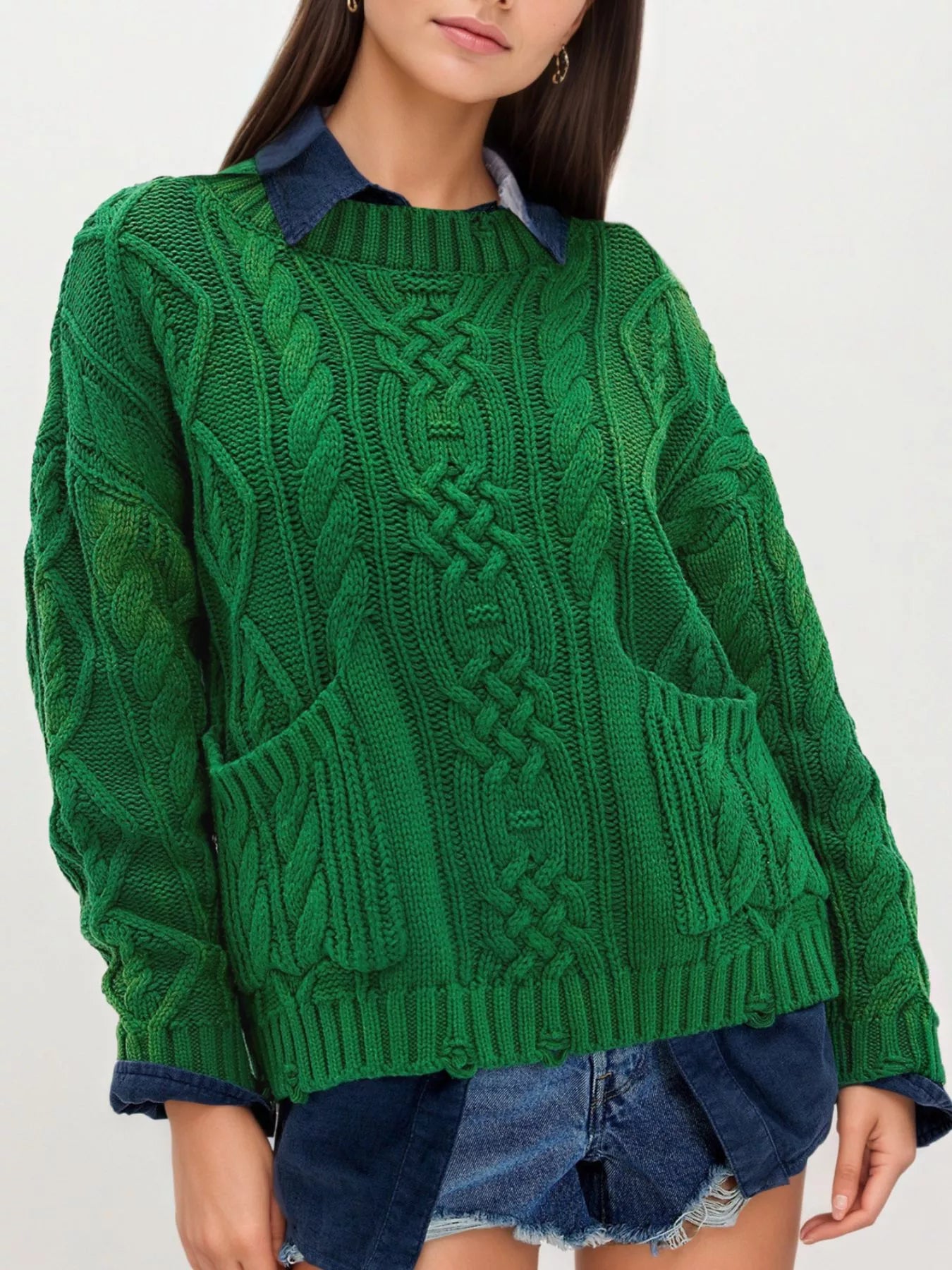 Front view of green cable knit sweater with front pockets layered over denim and shorts