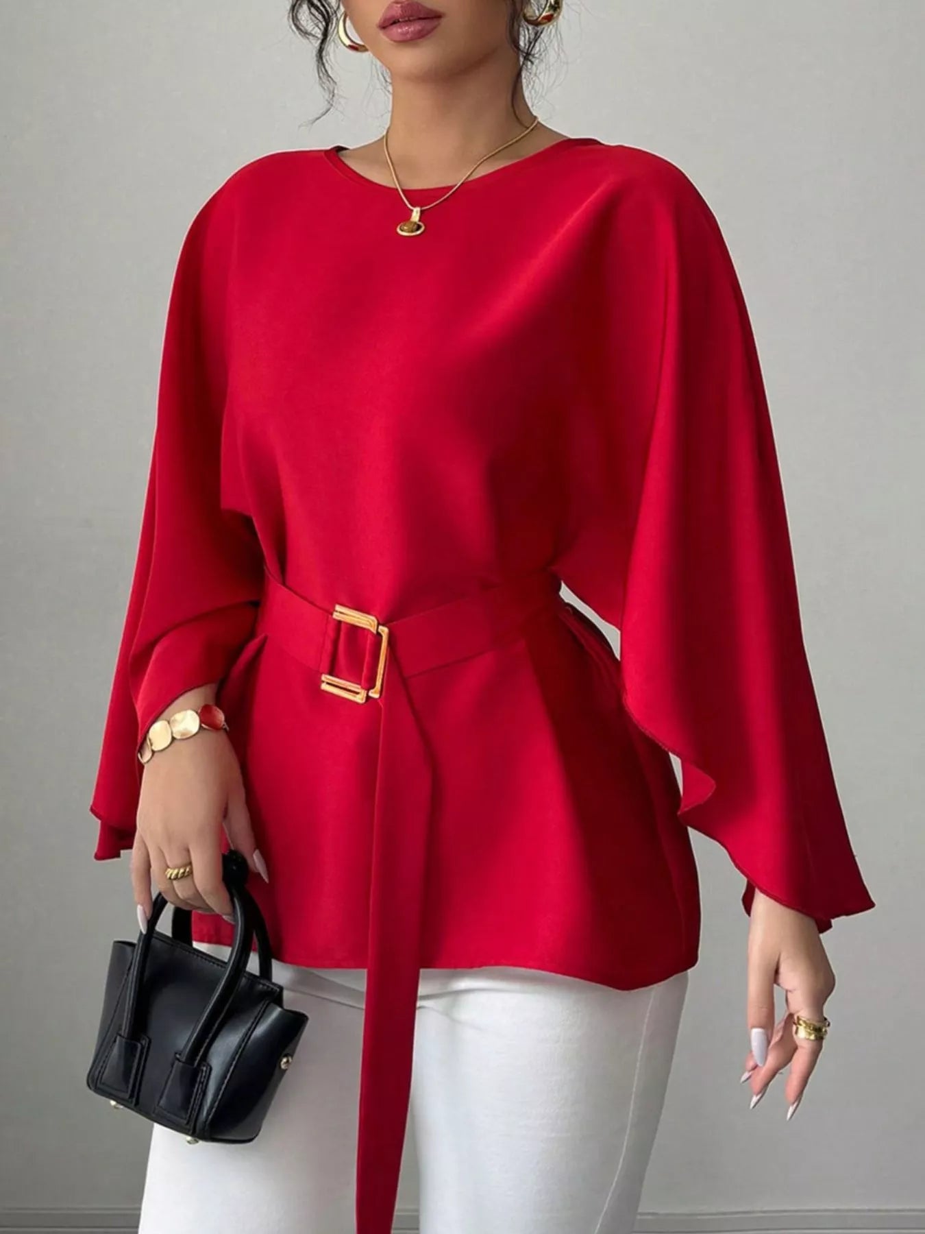Red round neck blouse close front view holding black handbag with gold buckle belt