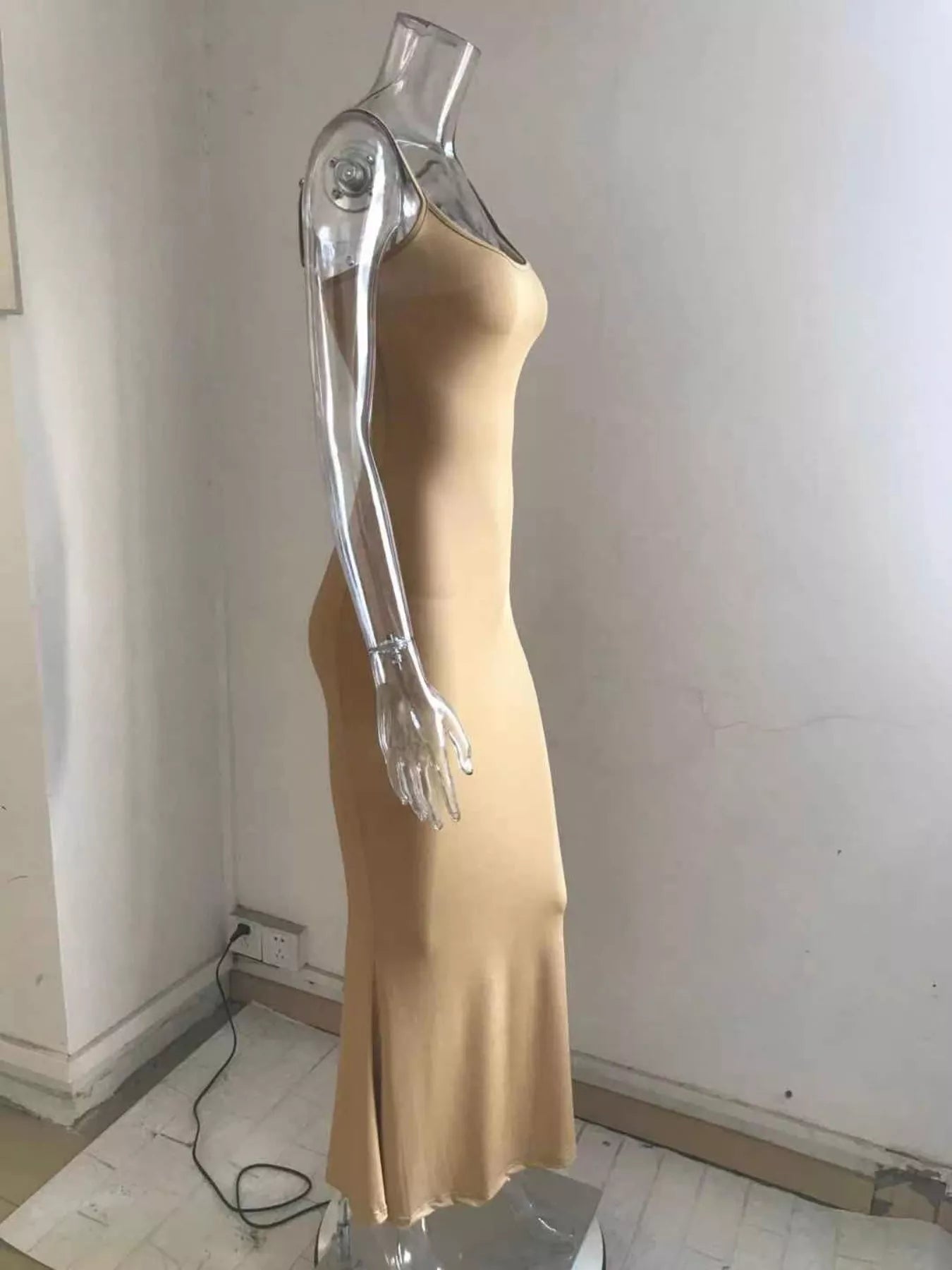 Side profile of a camel spaghetti strap bodycon maxi dress on a clear mannequin with a flared hem