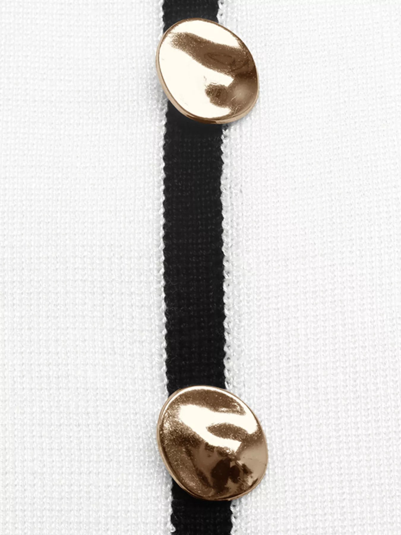 Close up of gold buttons on black placket of white knit top.
