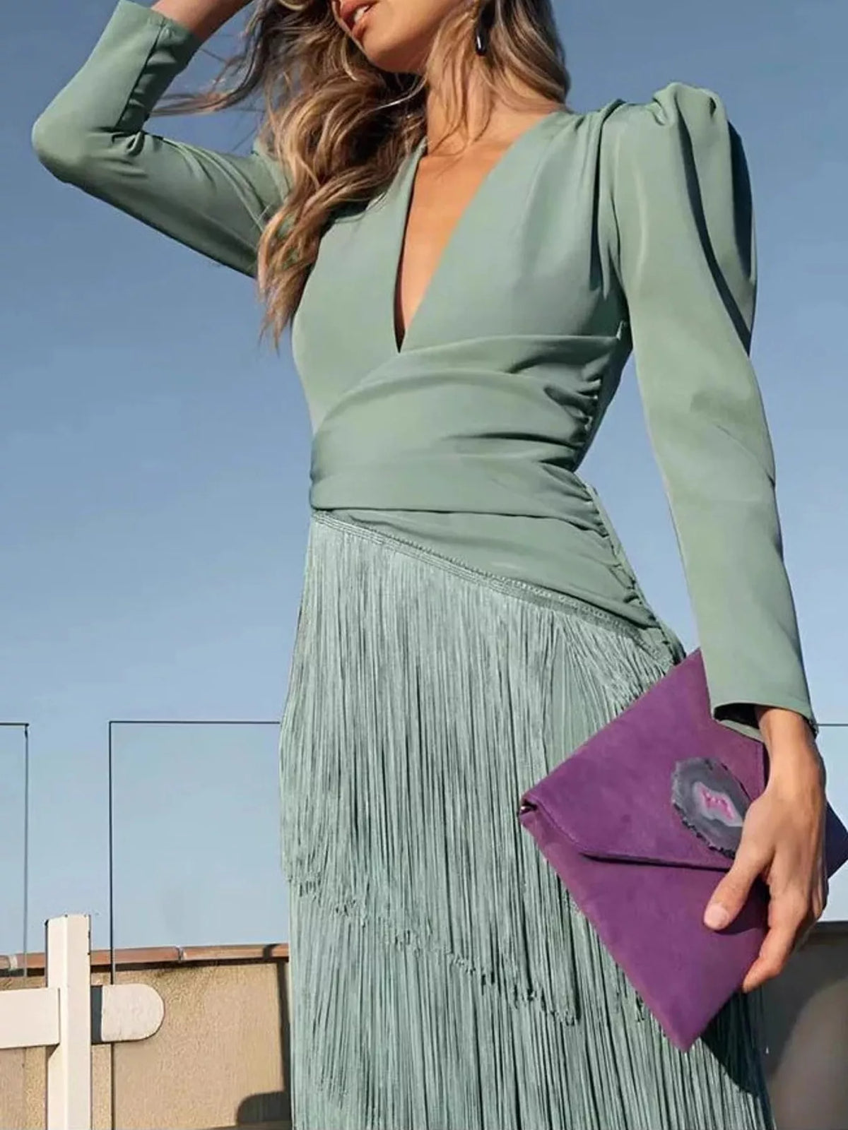 Close front view of a gum leaf green fringed maxi dress with puff sleeves and a purple clutch