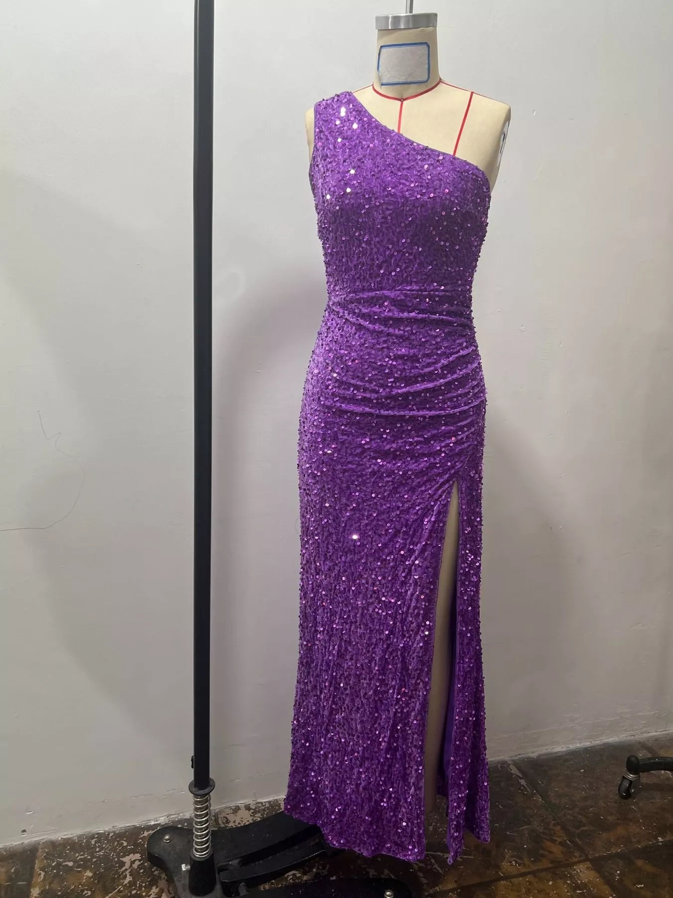 Purple sequin one shoulder evening dress shown front facing on a dress form with a high slit