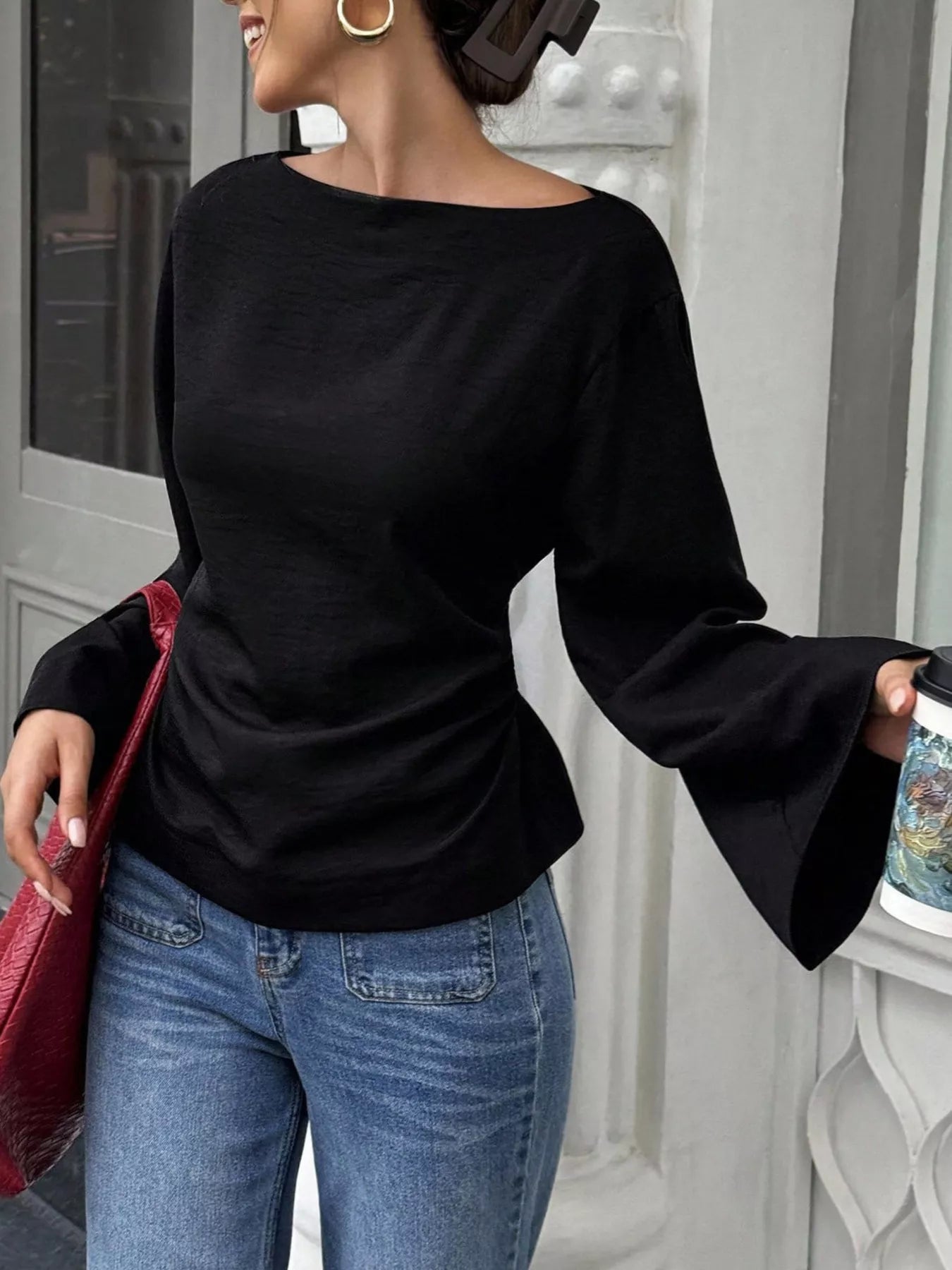 Angled front view of black boat neck long sleeve slim fit top holding a cup outdoors