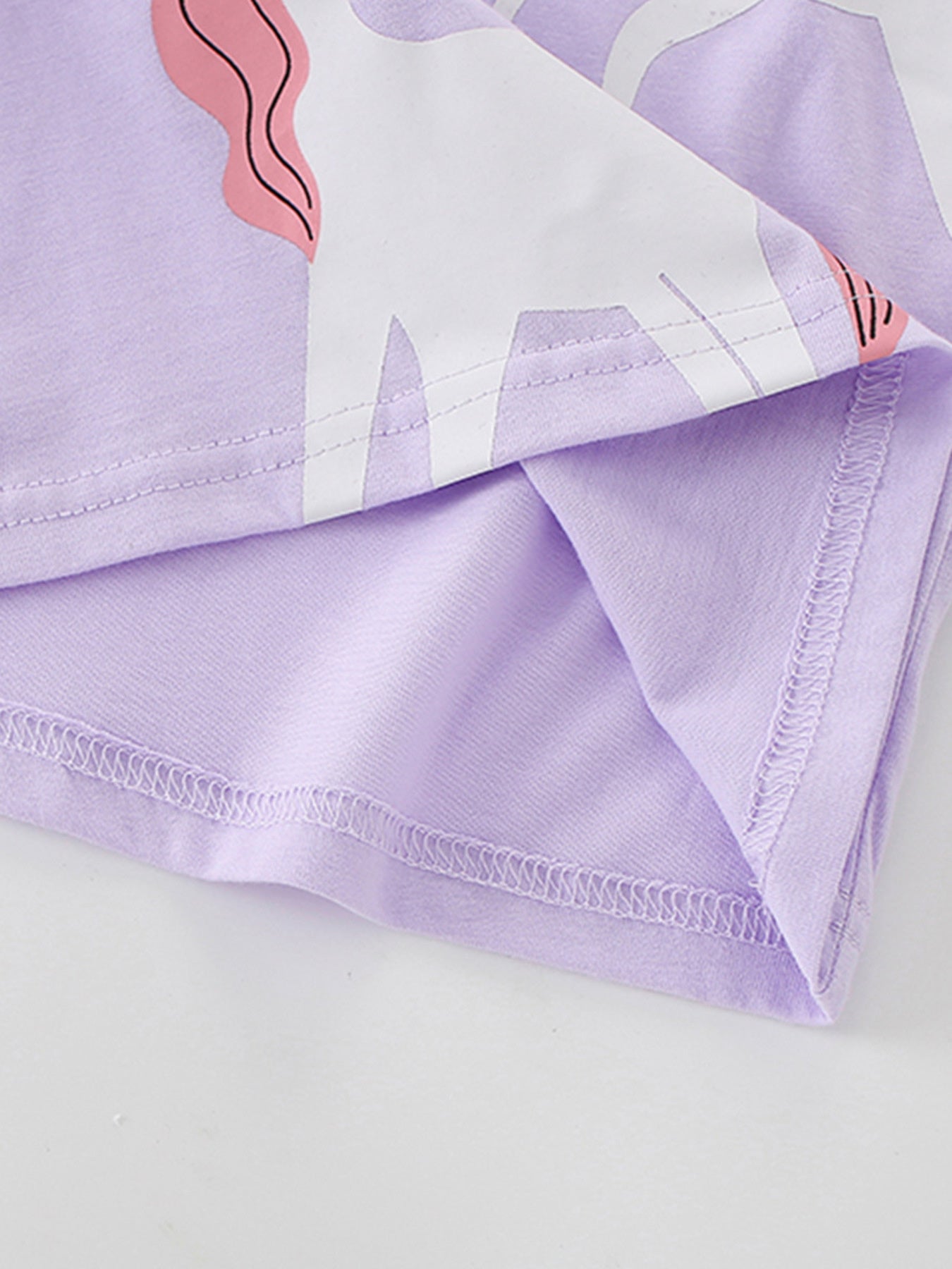 Close view of the stitched bottom hem and unicorn print edge on the light purple T-shirt