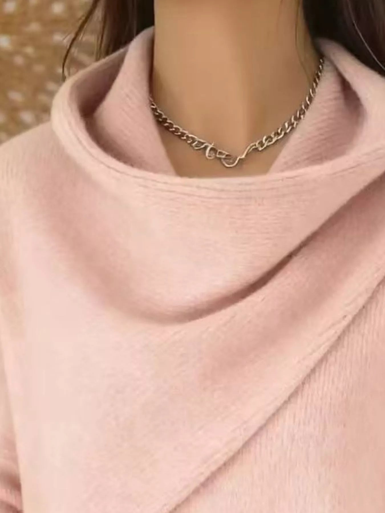 Close-up of the pale pink cowl neckline showing the draped asymmetric collar and fine knit texture