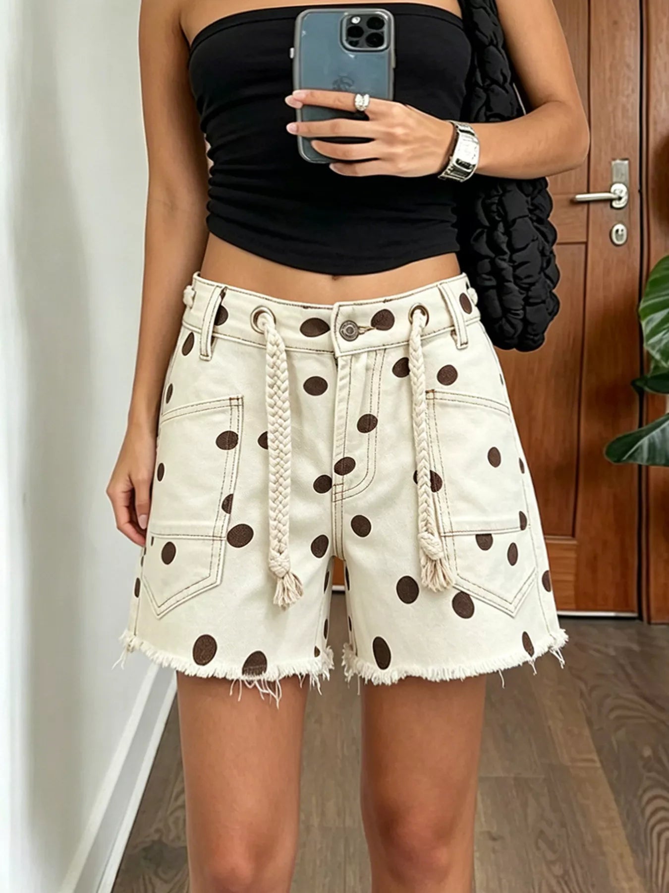 Women's polka-dot denim shorts with raw hems, pockets, and a braided drawstring.