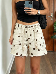 Women's polka-dot denim shorts with raw hems, pockets, and a braided drawstring.
