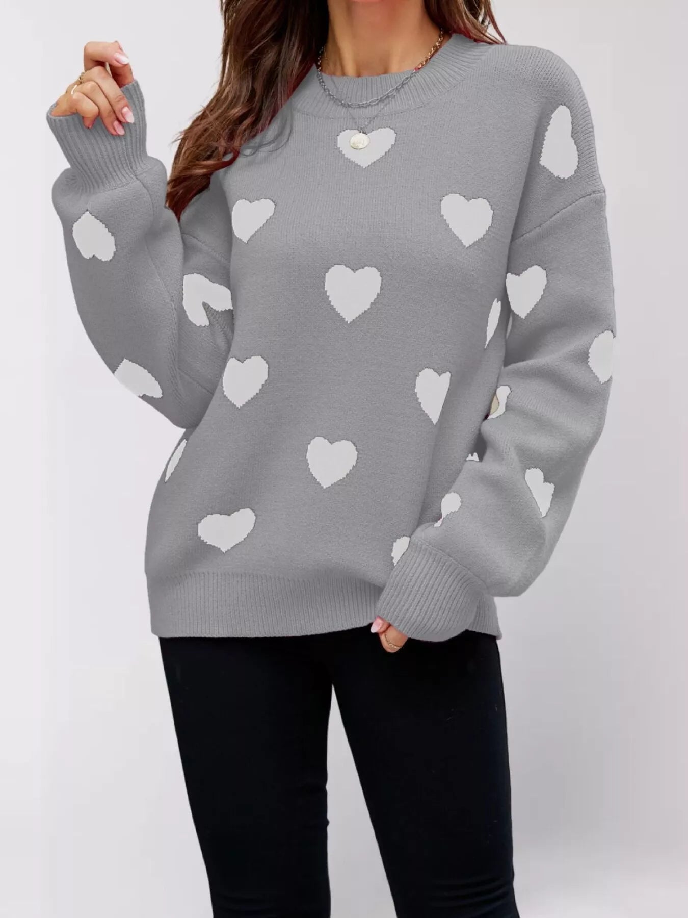 Front view of a gray dropped shoulder sweater with white hearts, one arm raised.