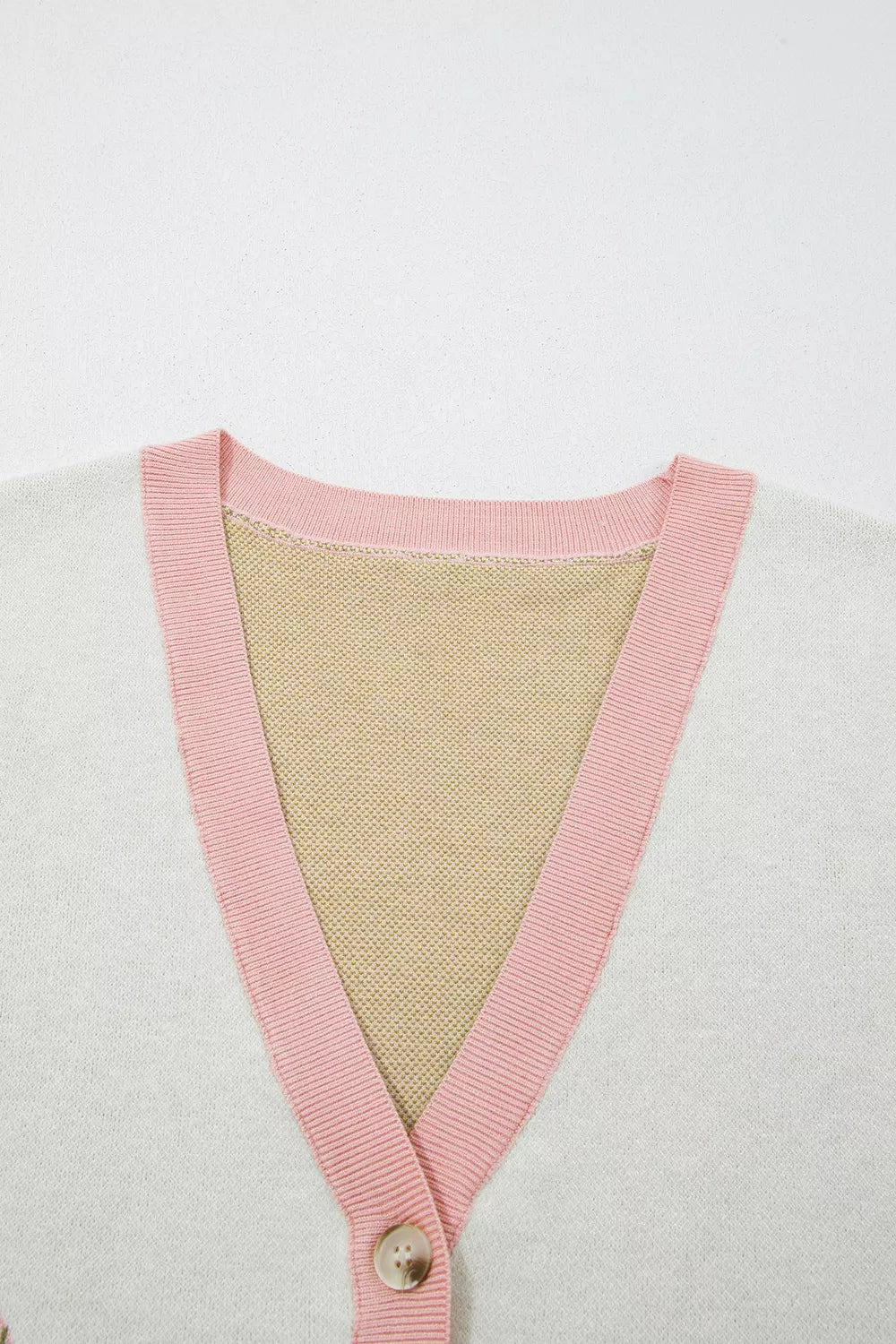 Close-up of the pink ribbed V neck and button on the cream cactus sweater vest