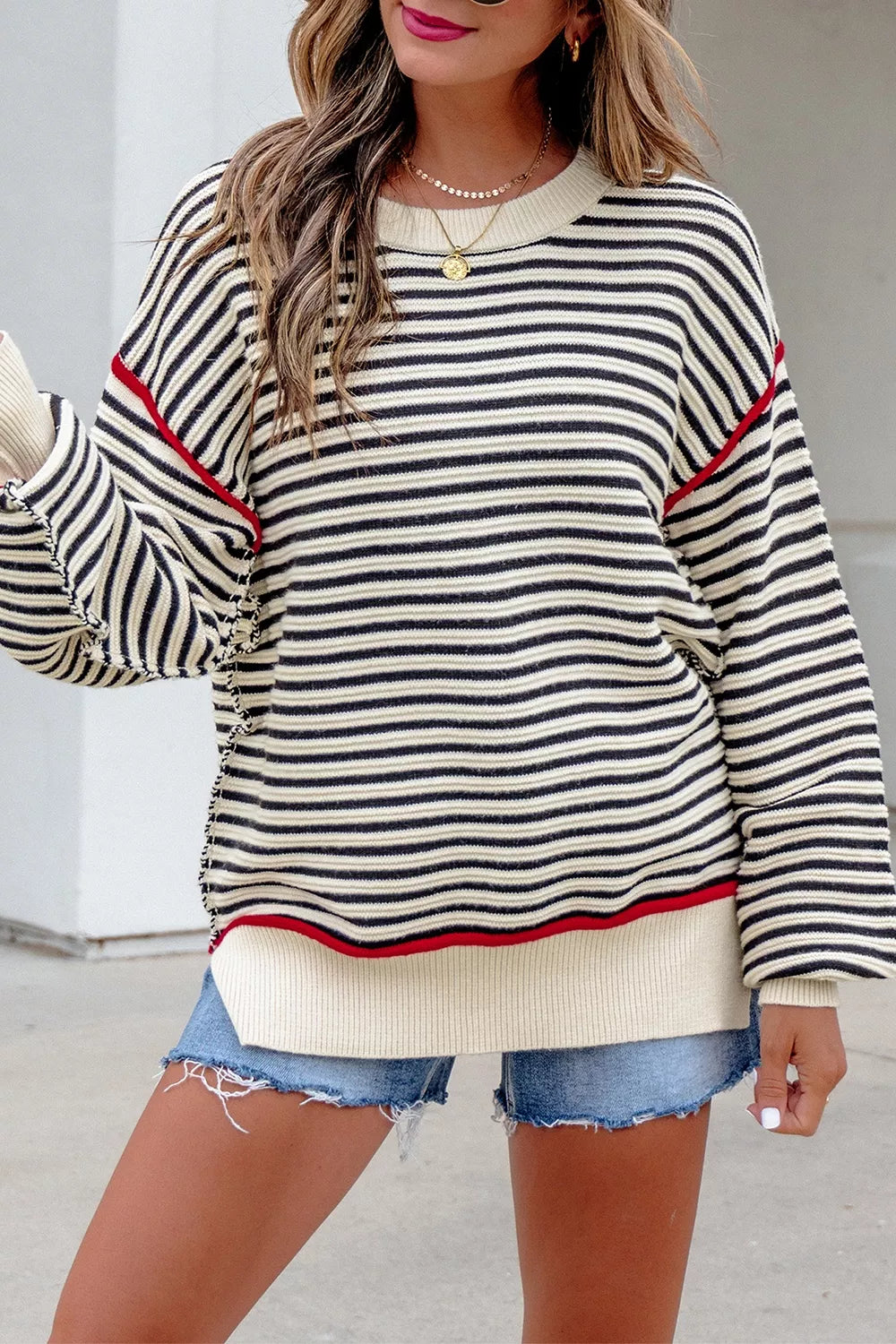 On-model front view of an oversized black and cream striped sweater with red seam accents