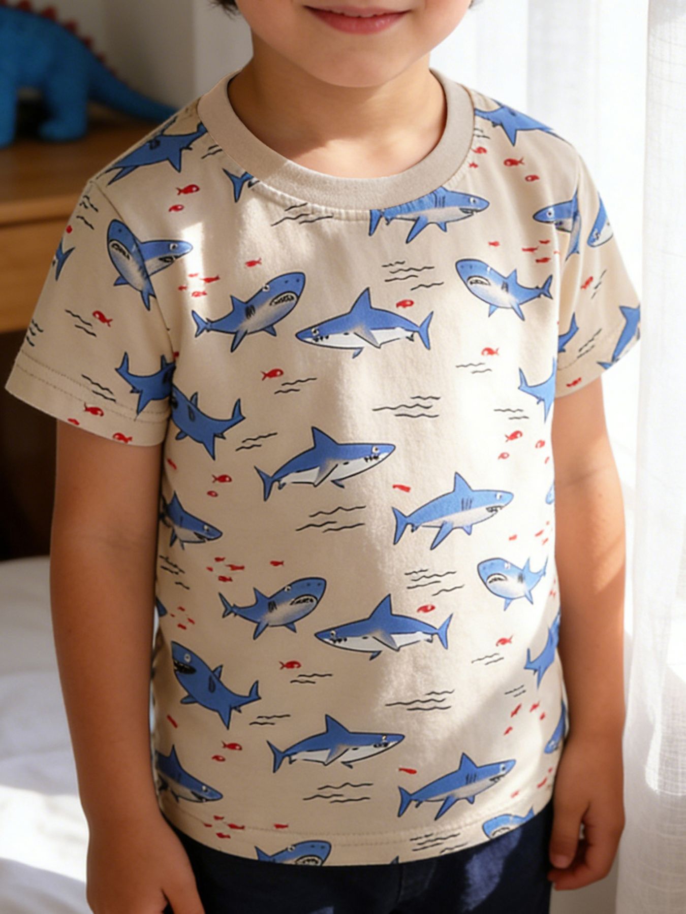 Front view of a children's crew neck t-shirt with blue shark and red fish print on beige fabric