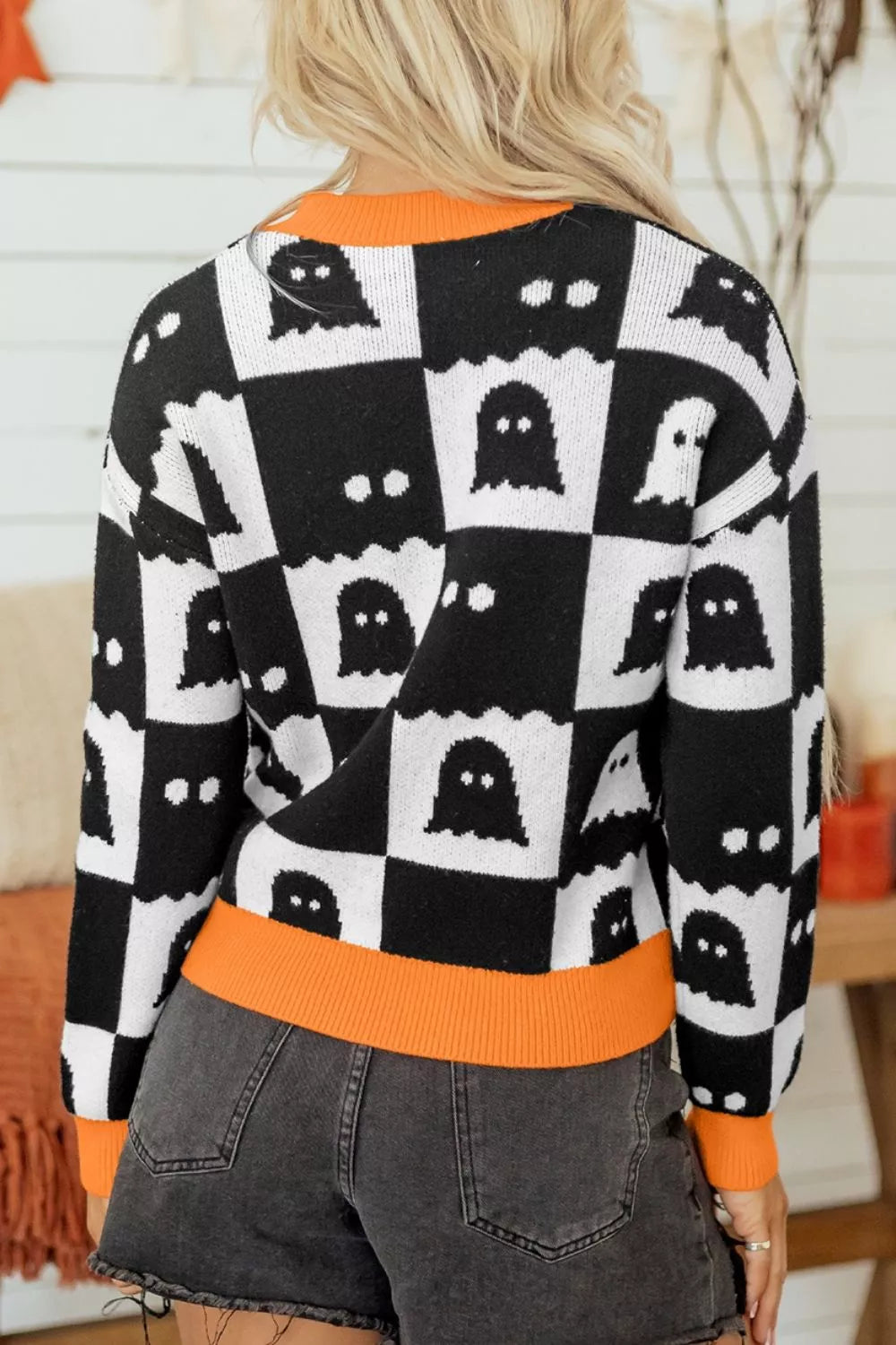 Back view of a black and white ghost checkerboard sweater with orange neck and hem