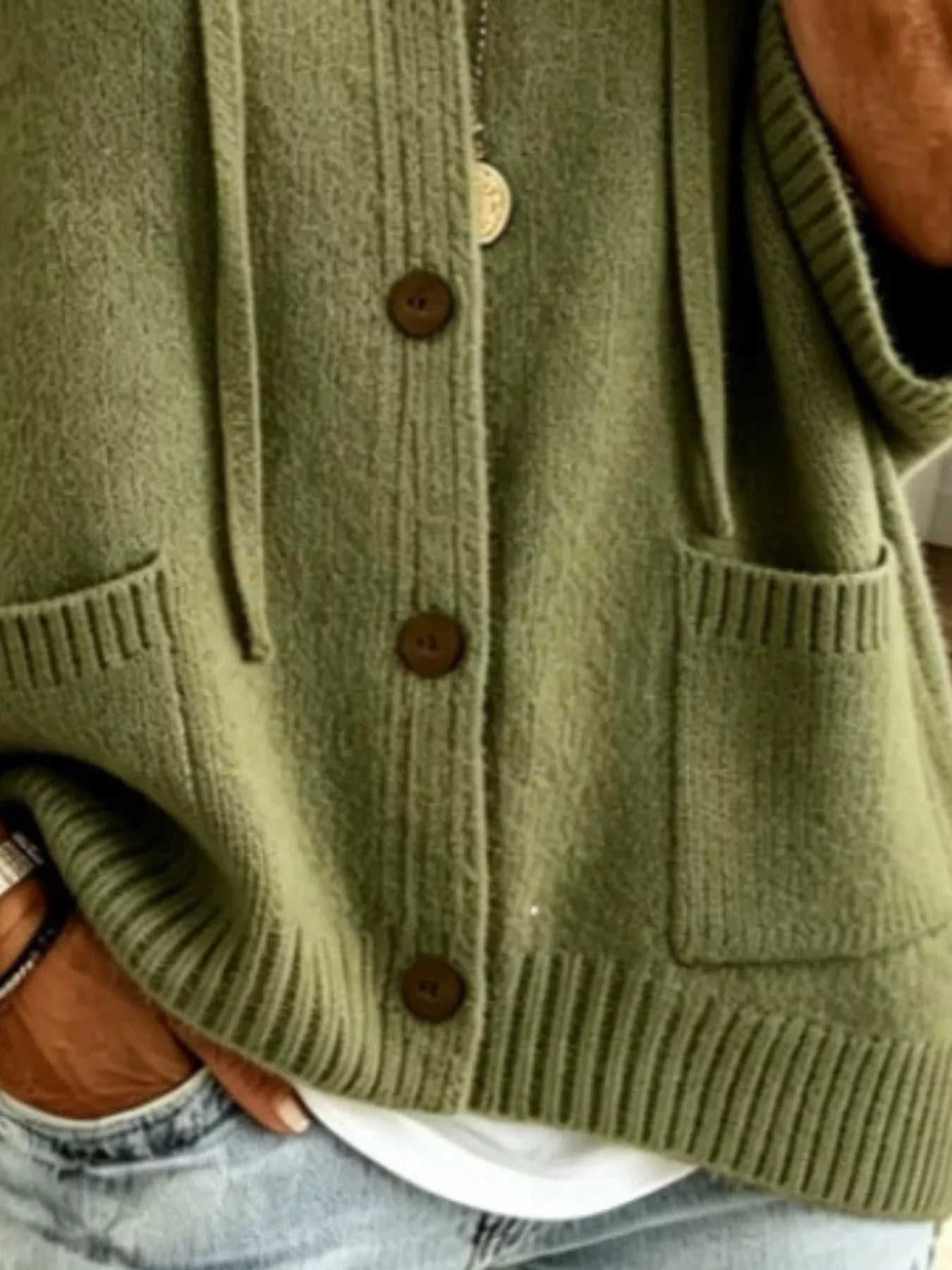 Detail view of the army green cardigan showing brown buttons, patch pockets and ribbed hem