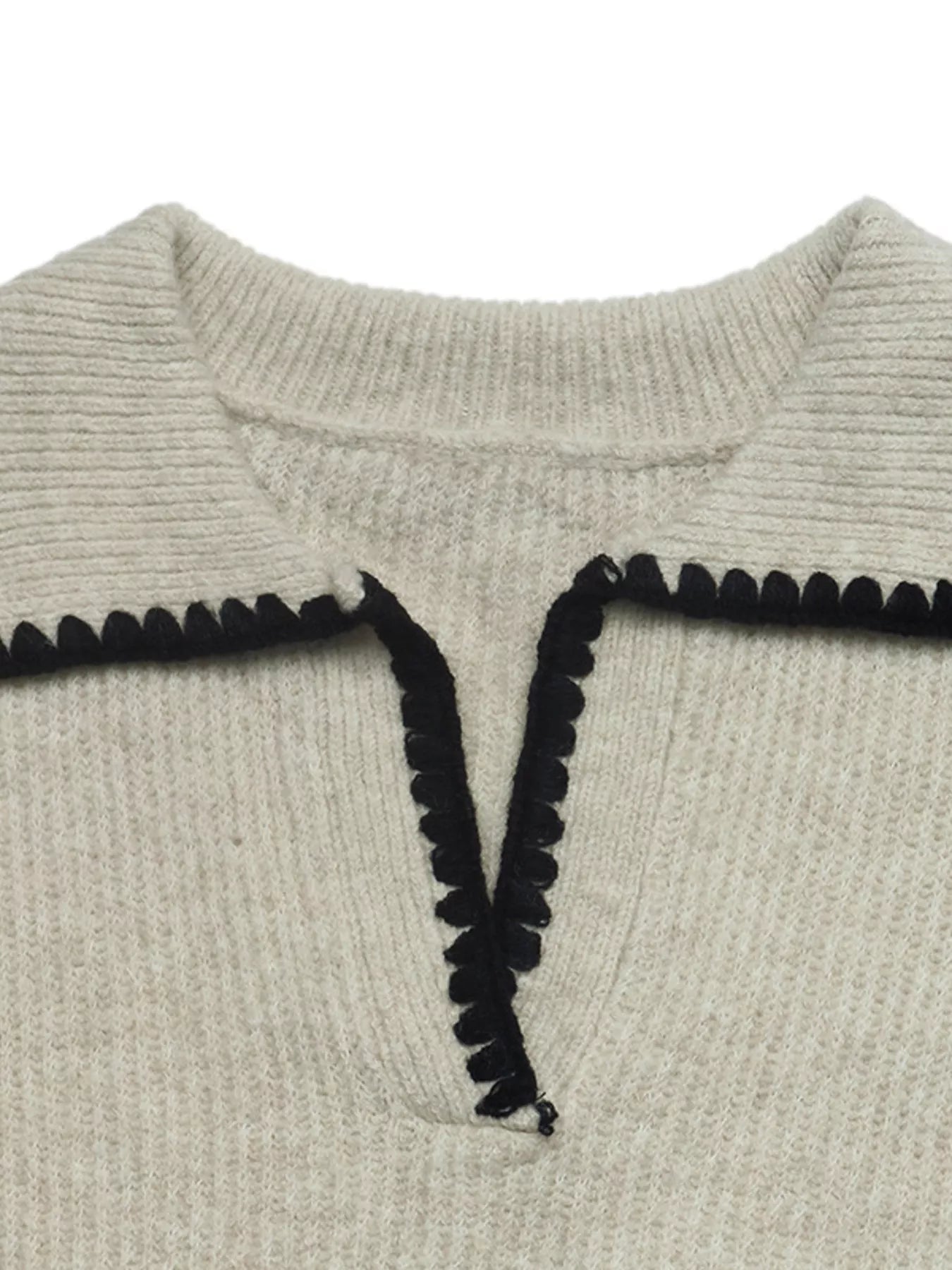 Close up of a cream sweater collar with black scalloped trim and V neckline