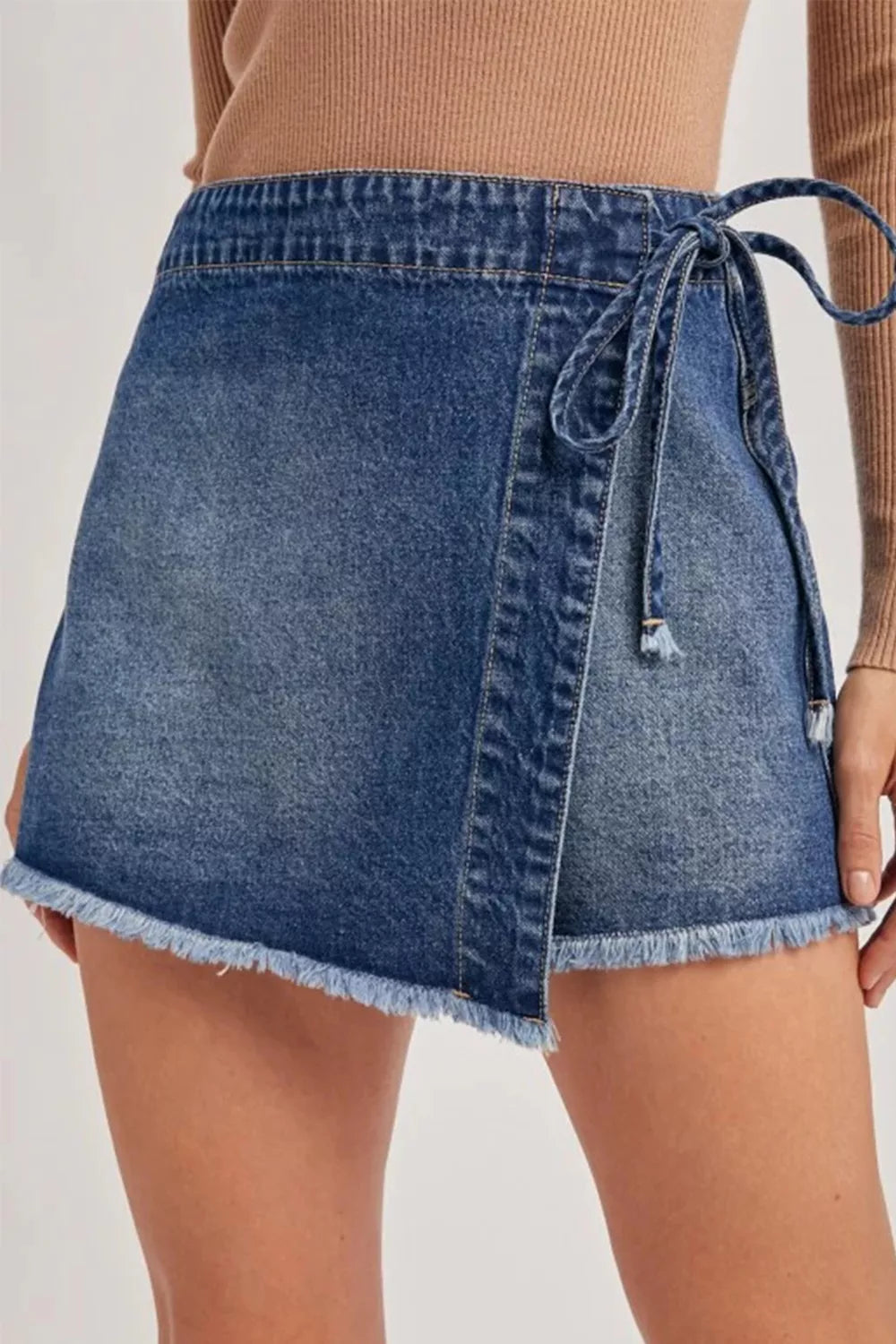 Women's wrap-front denim skort with a tied waist and raw hems.