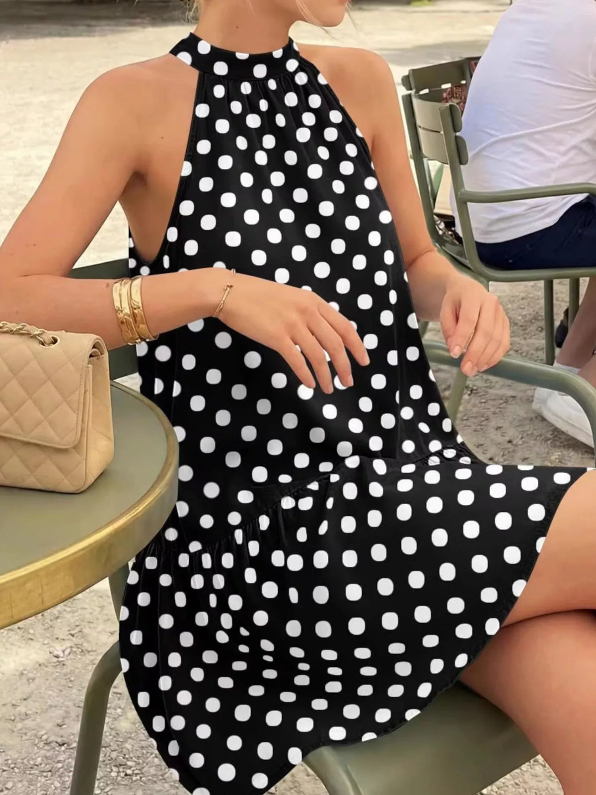 Black polka dot halter neck mini dress worn seated outdoors at a cafe table