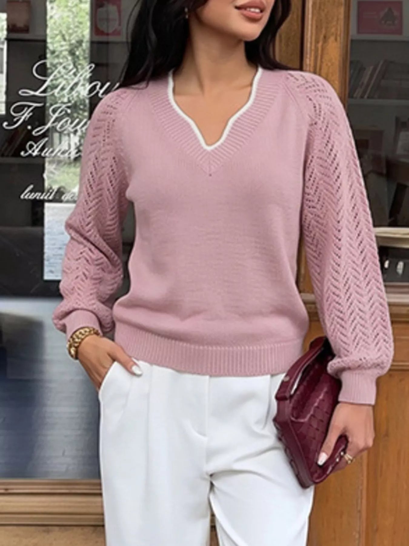 Standing front view of a pink V neck sweater with white trim and openwork long sleeves.