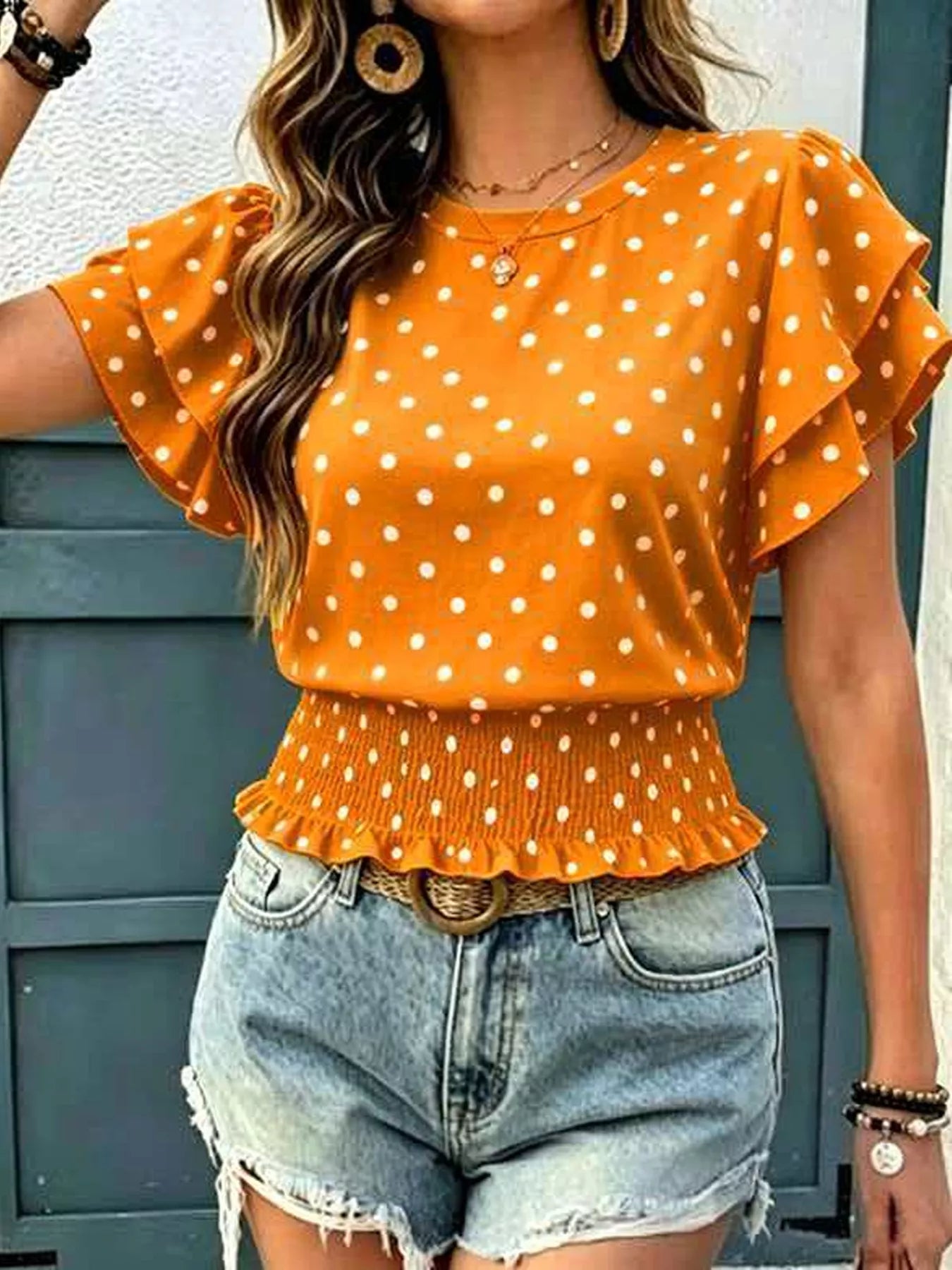 Orange polka dot blouse with ruffle sleeves and smocked peplum waist, shown styled with denim shorts