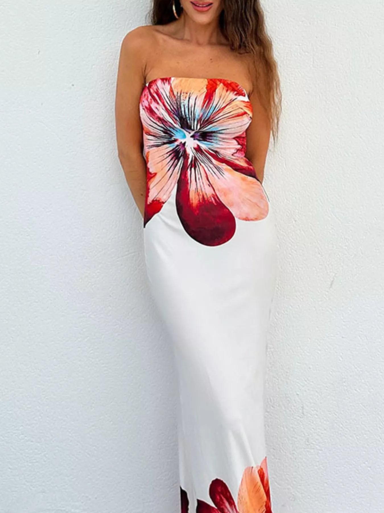 Strapless bodycon maxi dress with large floral print against a white wall, hands behind back
