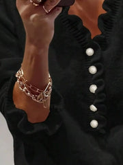 Close side view of a black ruffled sweater with pearl buttons