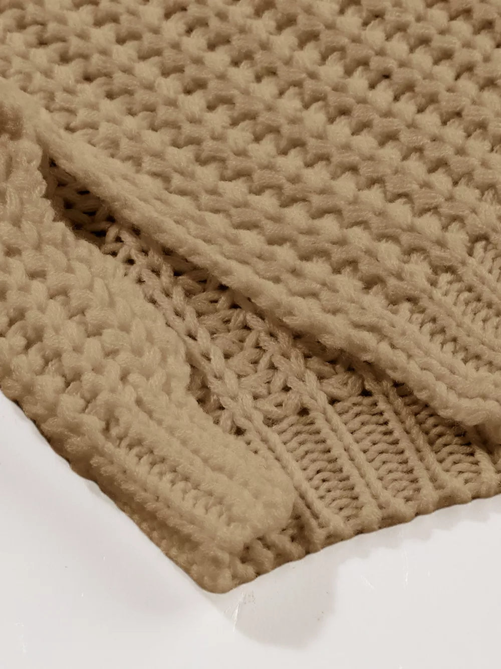 Close view of taupe chunky knit fabric and ribbed hem of a slouchy sweater.