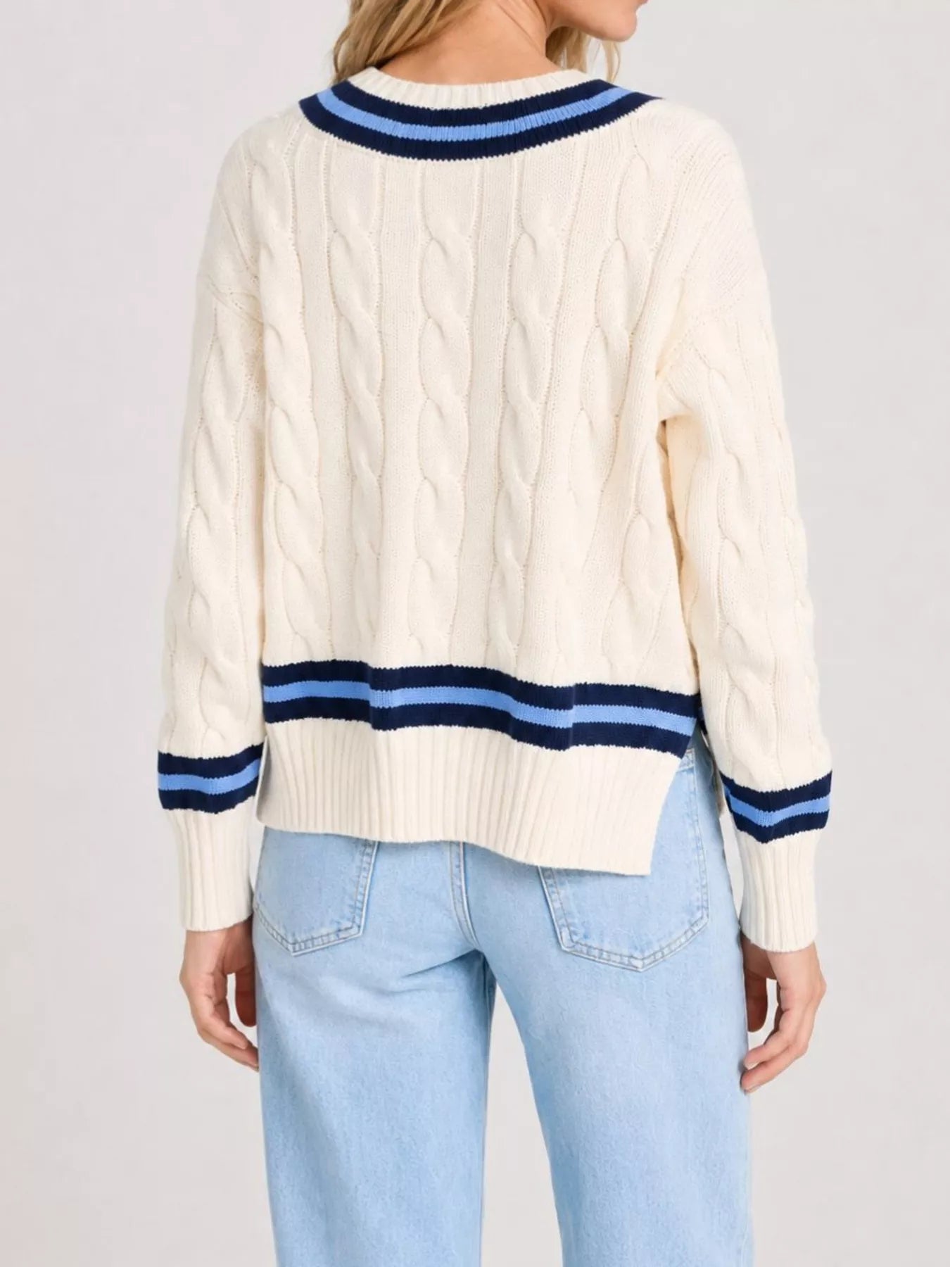 Back view of a cream cable knit sweater with navy and light blue striped trim