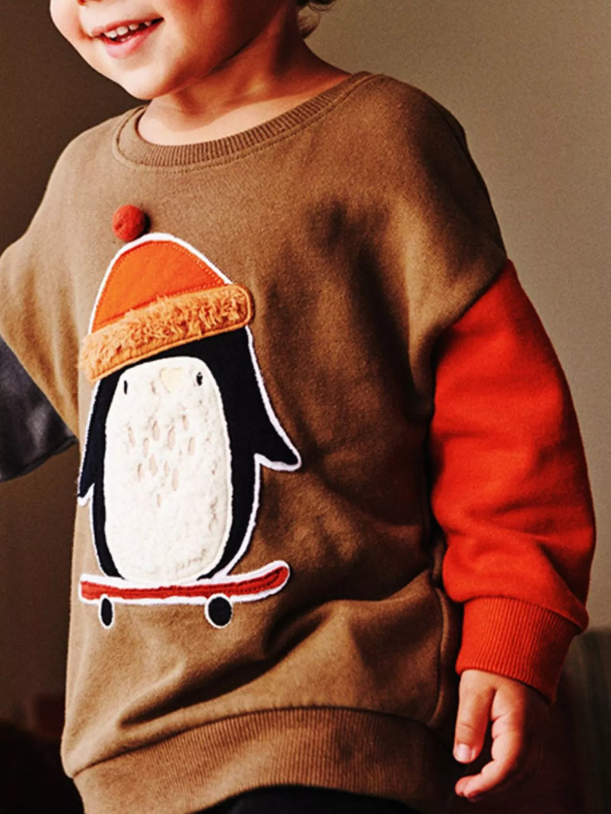 Side view of a children's caramel sweatshirt with a penguin on a skateboard wearing an orange hat